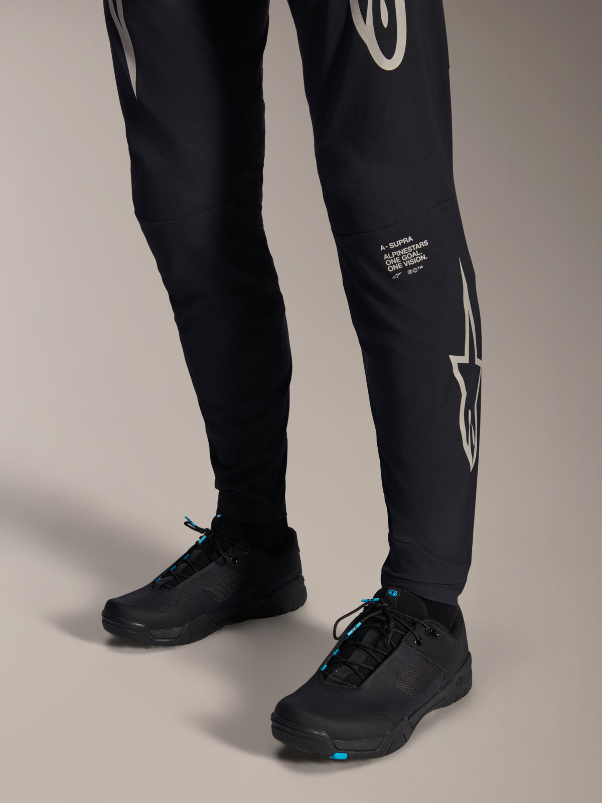 Alpinestars A-Supra Melt Pants, Black Mountain Bike Pants, featuring white Alpinestars wordmark and logo on the leg, worn with black cycling shoes with blue accents, performance off-road gear