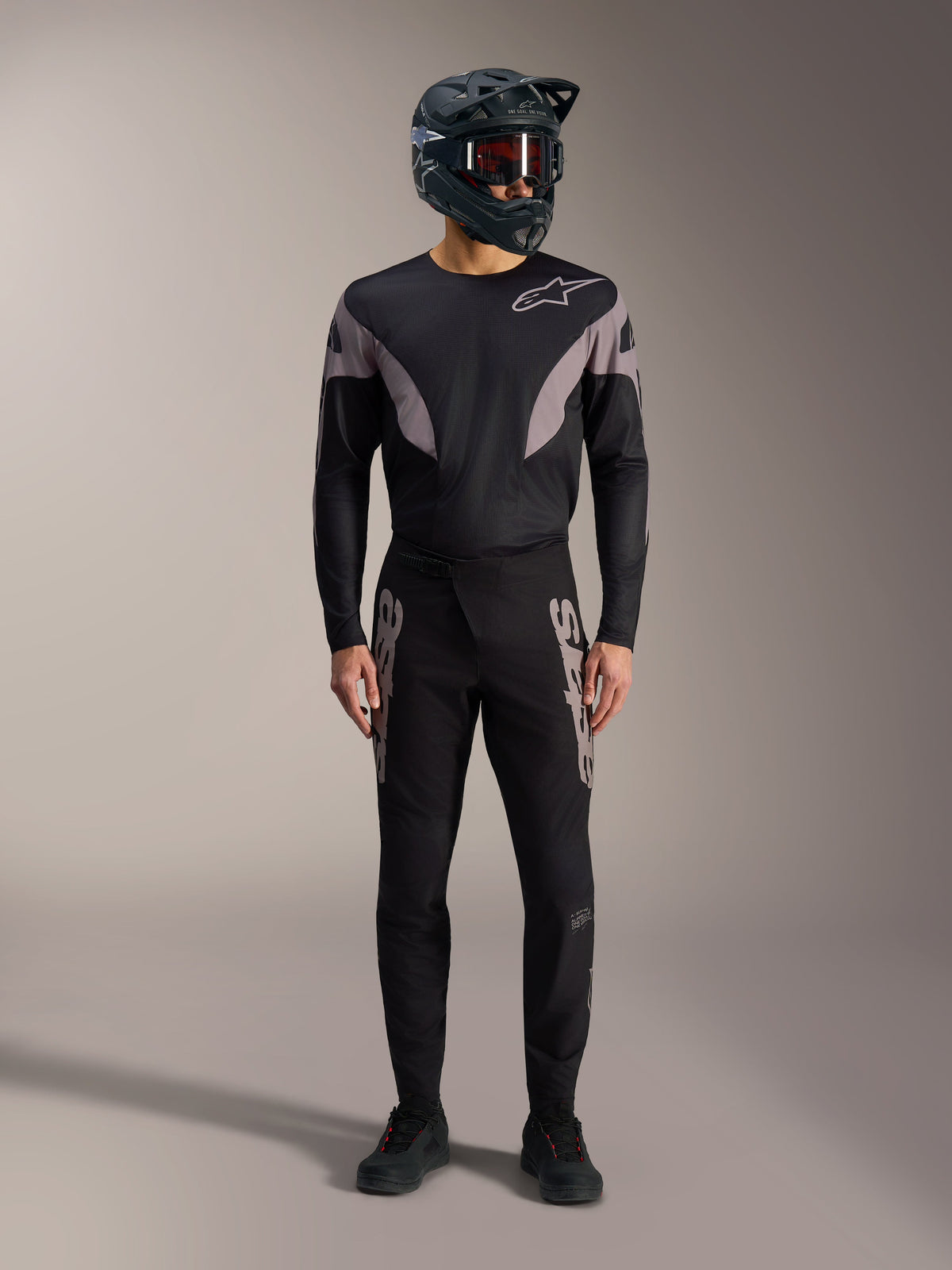Tenue VTT Alpinestars A-Supra Elite noire : maillot manches longues, pantalon de course à logos gris et casque intégral.