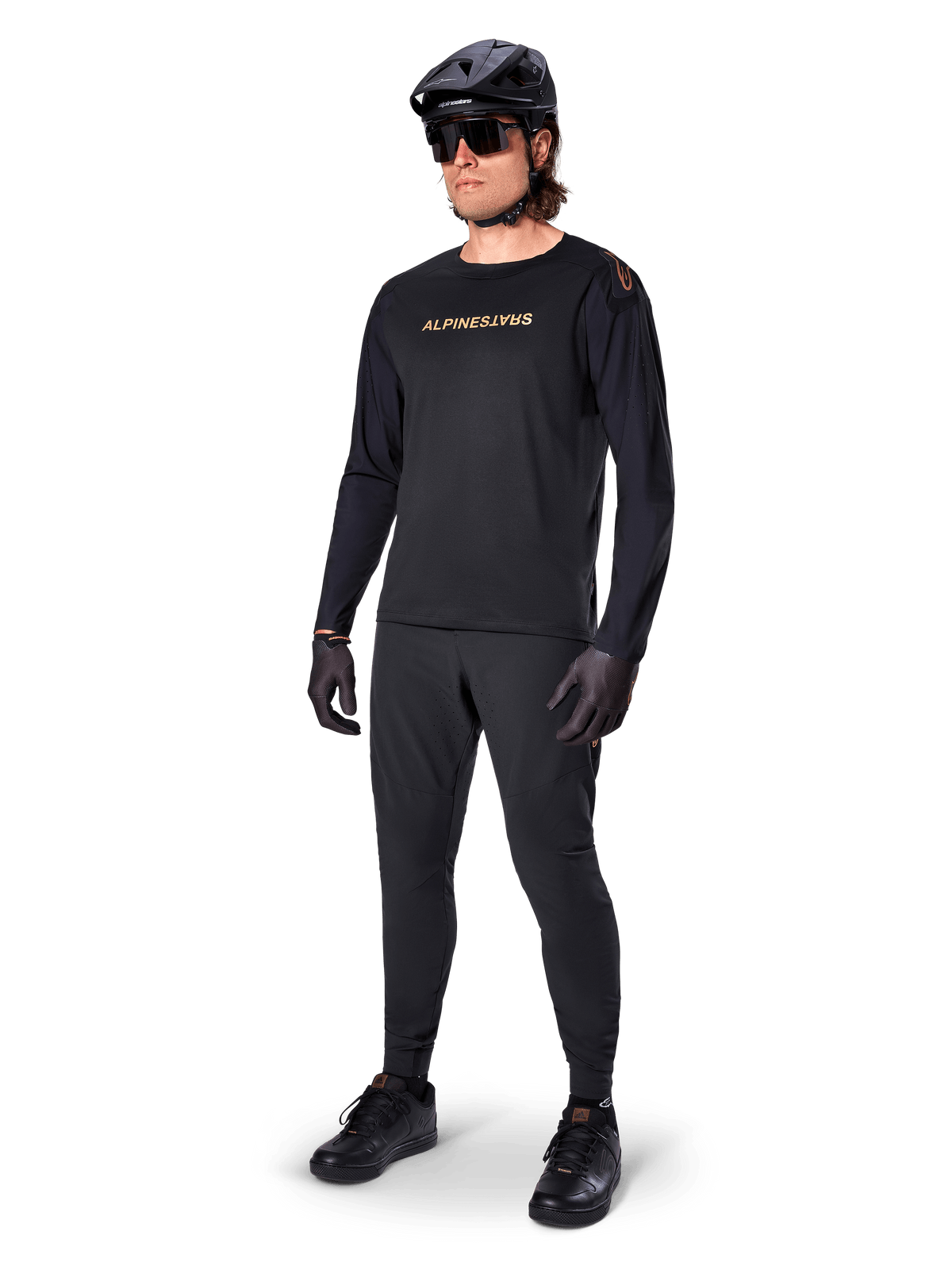 Maillot à manches longues Alpinestars A-Aria Polartec Switch, noir, logo bronze sur la poitrine, porté par un vététiste avec un casque noir et des lunettes de soleil, équipement de cyclisme haute performance pour le trail