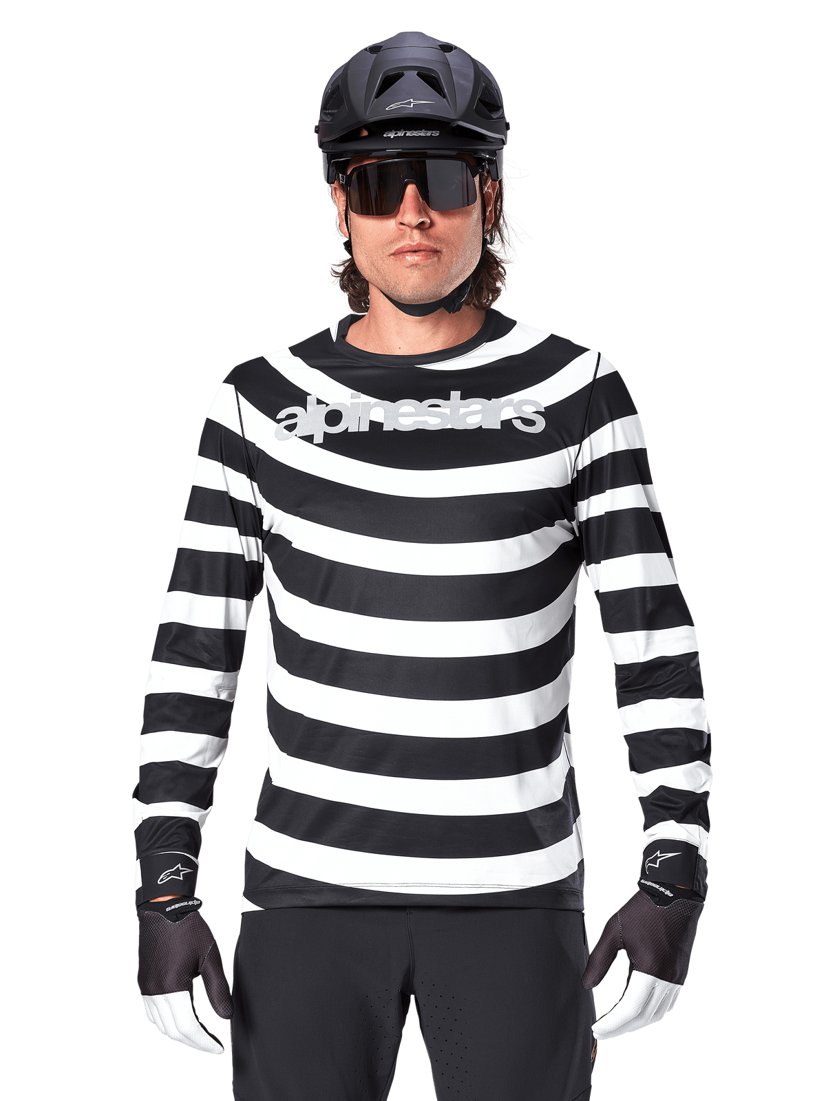 Male cyclist wearing Alpinestars A-Aria Oscar Long Sleeve Jersey, Black and White horizontal stripes, reflective Alpinestars logo on the chest, styled with a black MTB helmet, cycling sunglasses, and performance gloves