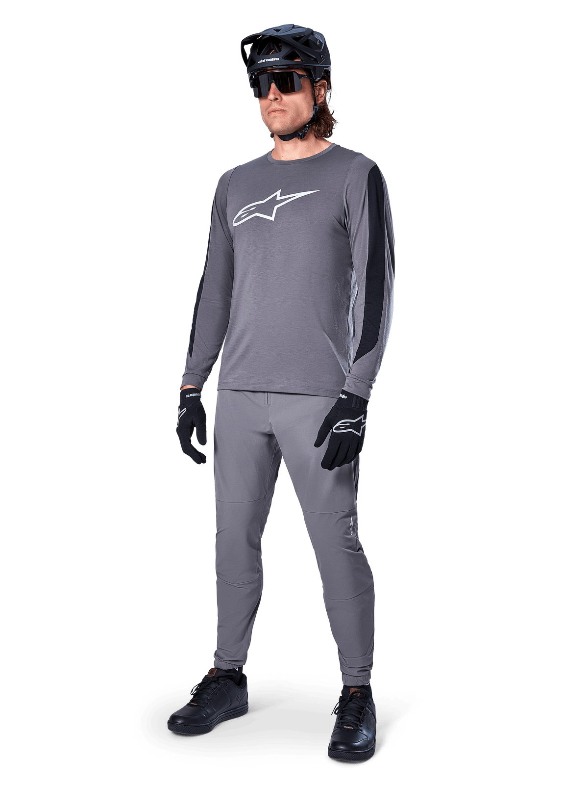 Alpinestars A-Dura Dri Astar Jersey, maillot de VTT à manches longues, gris foncé avec logo blanc sur la poitrine, panneaux en maille noire sur les manches, porté avec un pantalon gris assorti, un casque noir et des gants, équipement de VTT haute performance