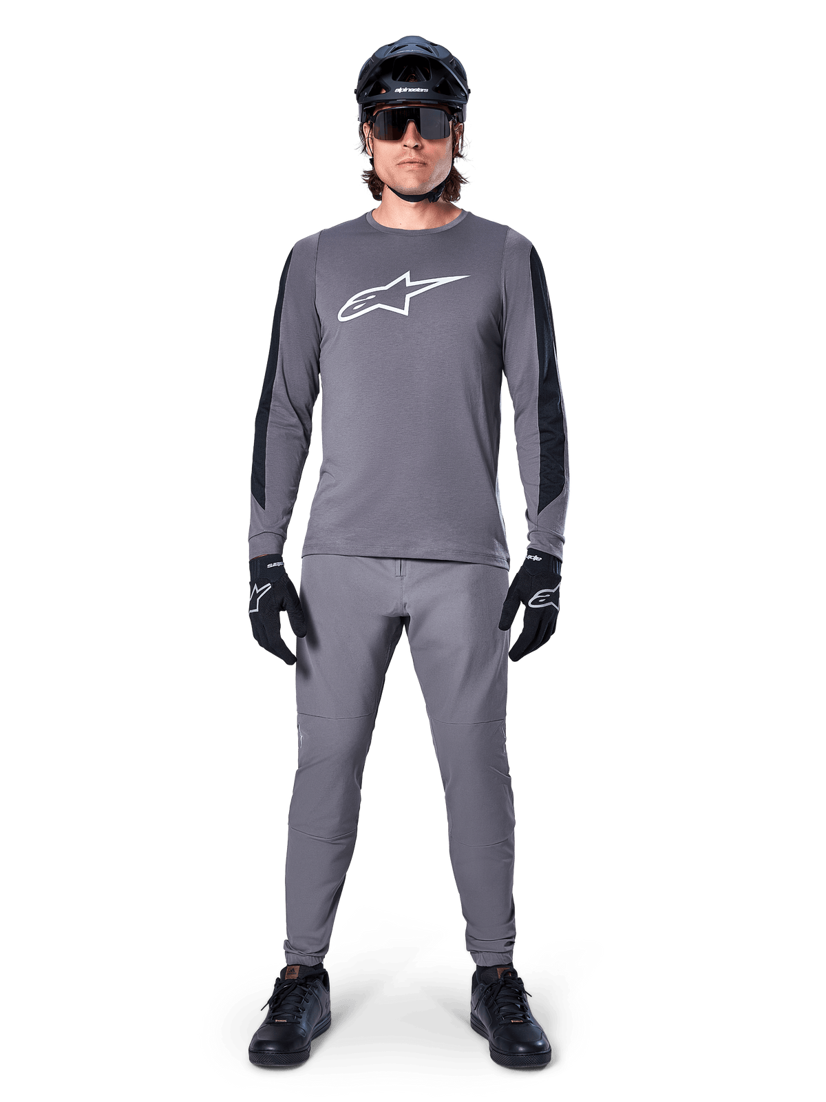 Maillot Alpinestars A-Dura Dri Astar à manches longues, maillot de VTT gris foncé avec logo blanc sur la poitrine et empiècements noirs sur les manches, porté avec un pantalon gris assorti, un casque noir, des lunettes de soleil et des gants pour une tenue de cyclisme tout-terrain complète