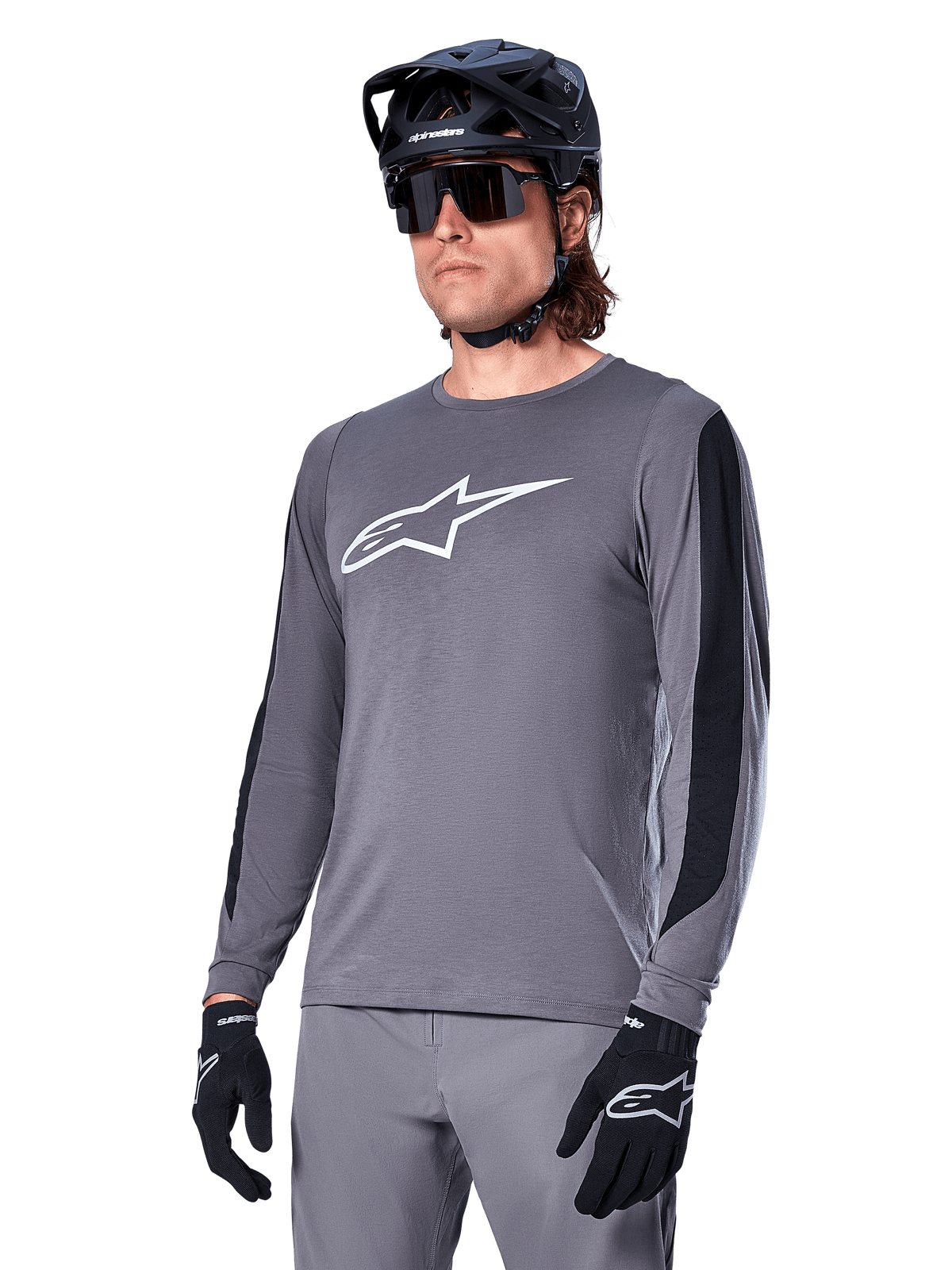 Alpinestars A-Dura Dri Astar Jersey à manches longues, gris foncé avec logo blanc sur la poitrine et panneaux latéraux en maille noire, maillot de VTT, porté avec un casque noir, des lunettes de soleil et un pantalon gris assorti