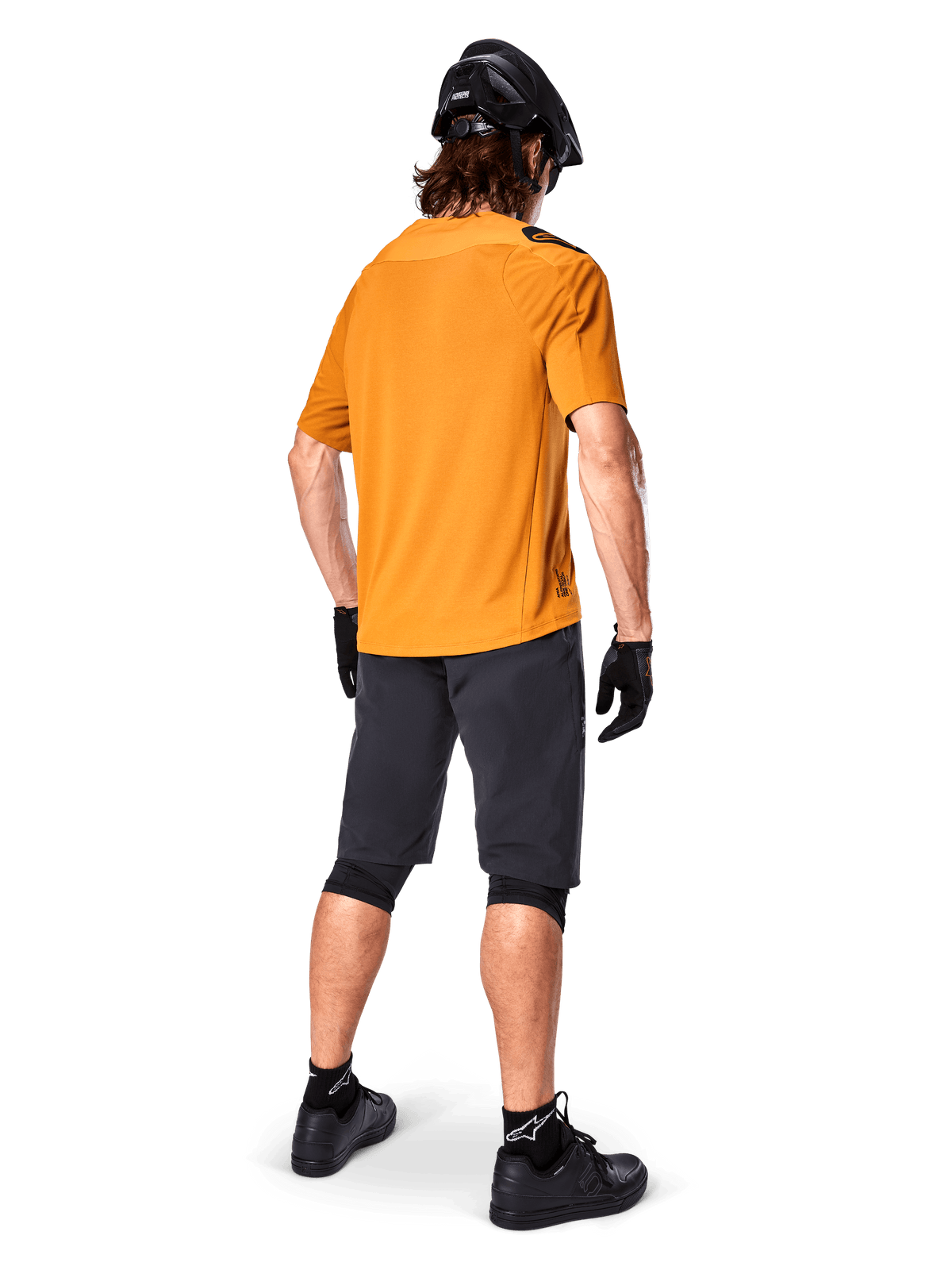 Alpinestars A-Aria Polartec Switch Jersey, maillot de VTT à manches courtes, Or foncé, vue arrière d'un modèle portant un short de VTT gris foncé, un casque noir et des gants, vêtements de cyclisme techniques pour les sentiers tout-terrain