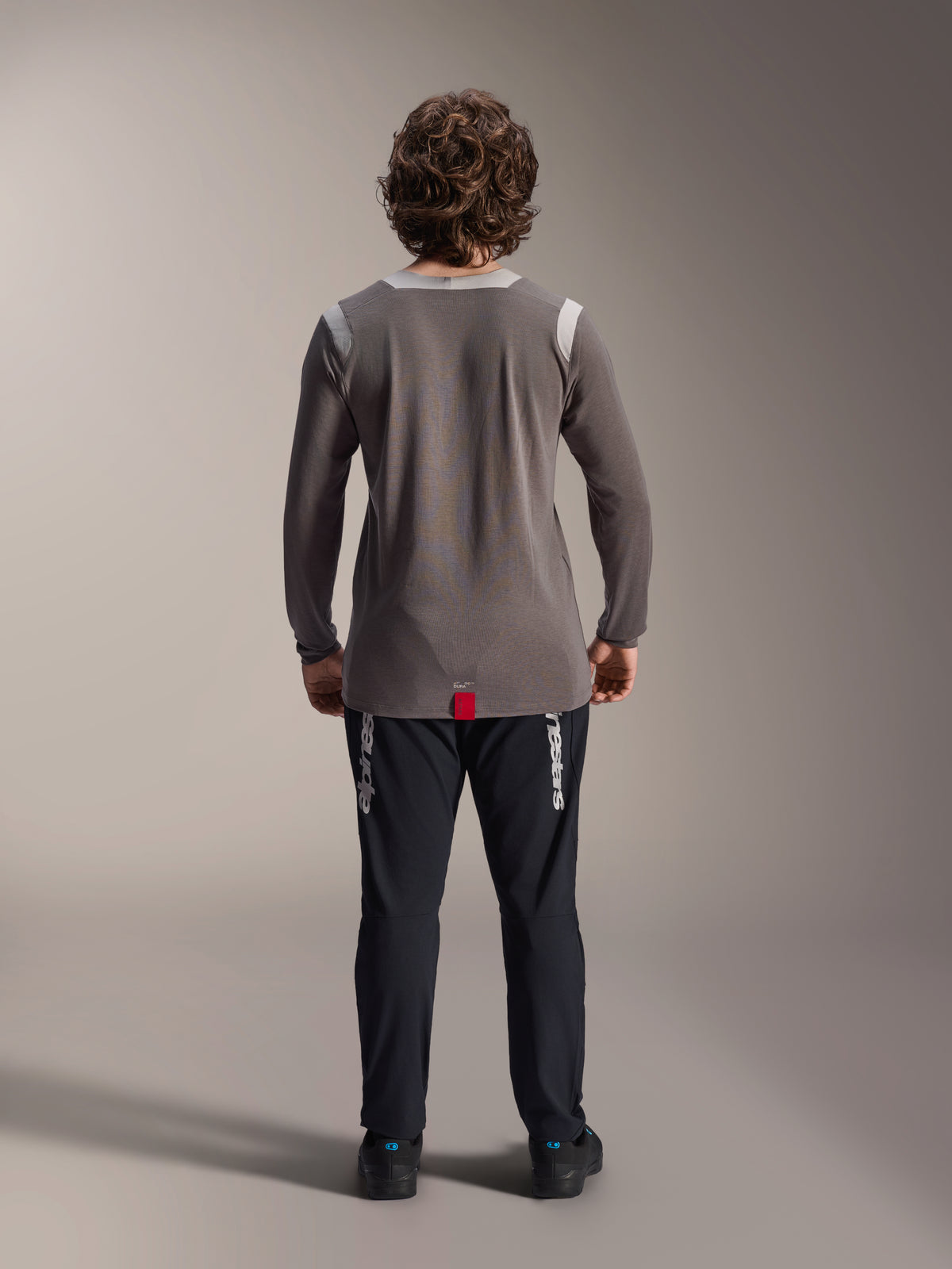 Pantalon Alpinestars A-Dura Elite et maillot à manches longues A-Dura Dri Wool, pantalon noir avec marquage blanc, maillot technique gris, vue arrière d'une tenue de VTT, vêtements de cyclisme tout-terrain durables