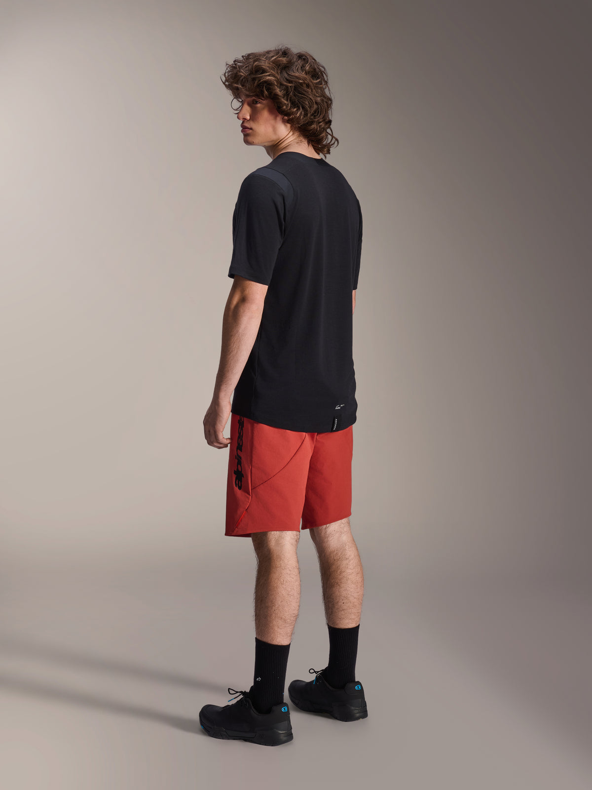Short Alpinestars A-Dura Elite, short de VTT, orange foncé, porté avec un maillot noir à manches courtes et des chaussures de VTT noires, vue latérale arrière du mannequin mettant en valeur la coupe performance et le logo