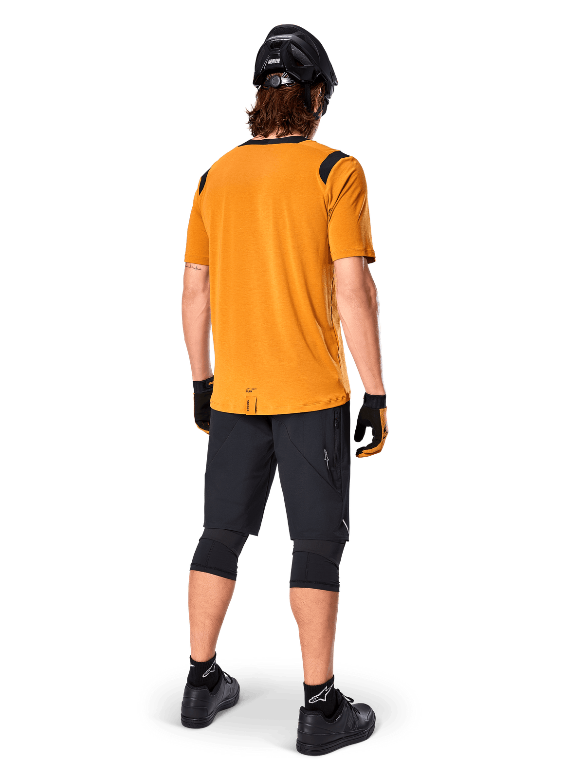 Maillot à manches courtes Alpinestars A-Dura Dri Wool, maillot de cyclisme, or foncé, vue arrière d'un vététiste portant un maillot jaune moutarde avec des accents en maille noire aux épaules, associé à un short noir, des genouillères, un casque noir et des gants, équipement technique de cyclisme tout-terrain