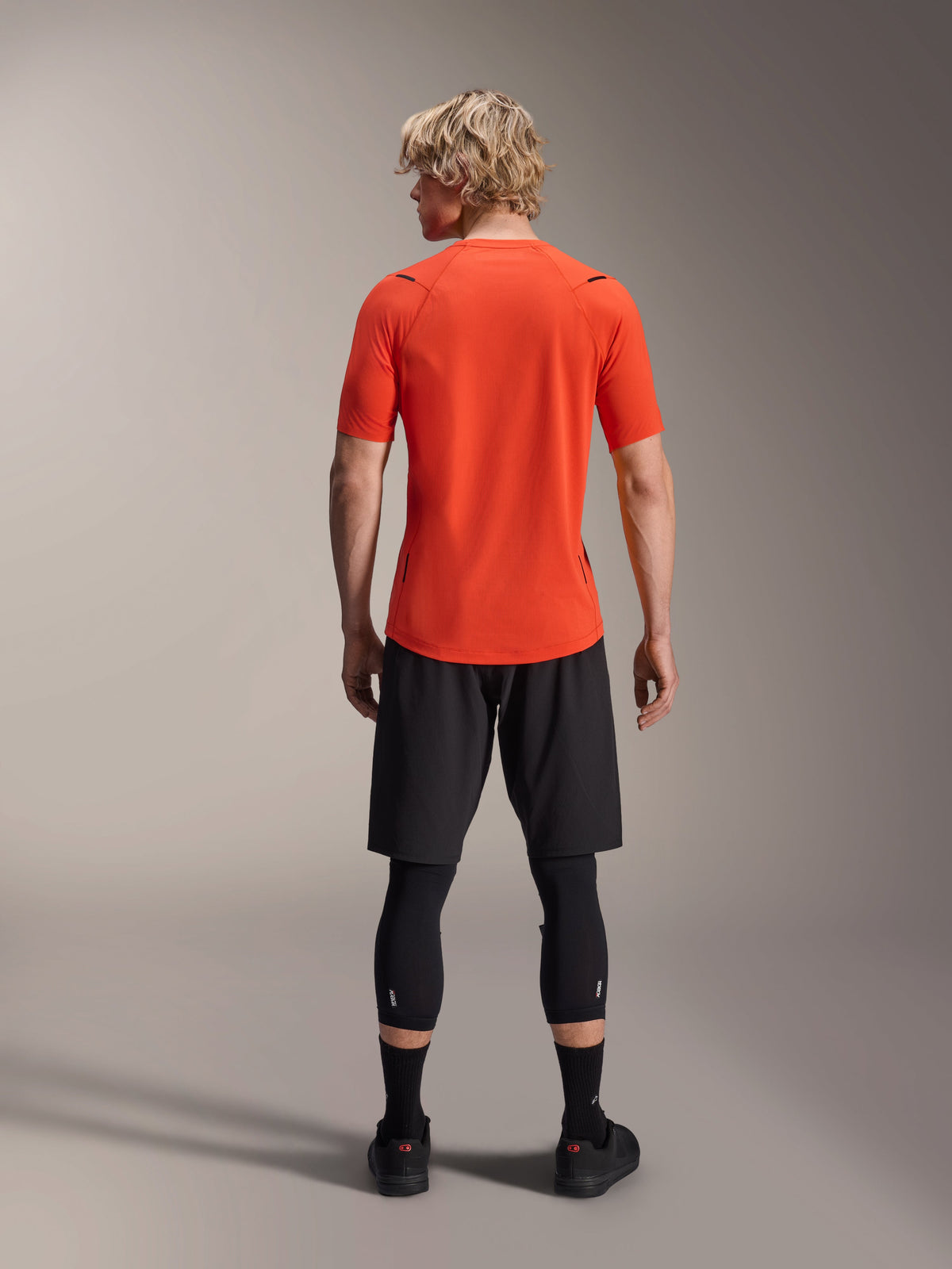 Alpinestars A-Aria Astar Jersey, Short Sleeve MTB Jersey, Spicy Orange, back view showing performance fit and longer drop tail, paired with black cycling shorts and leggings