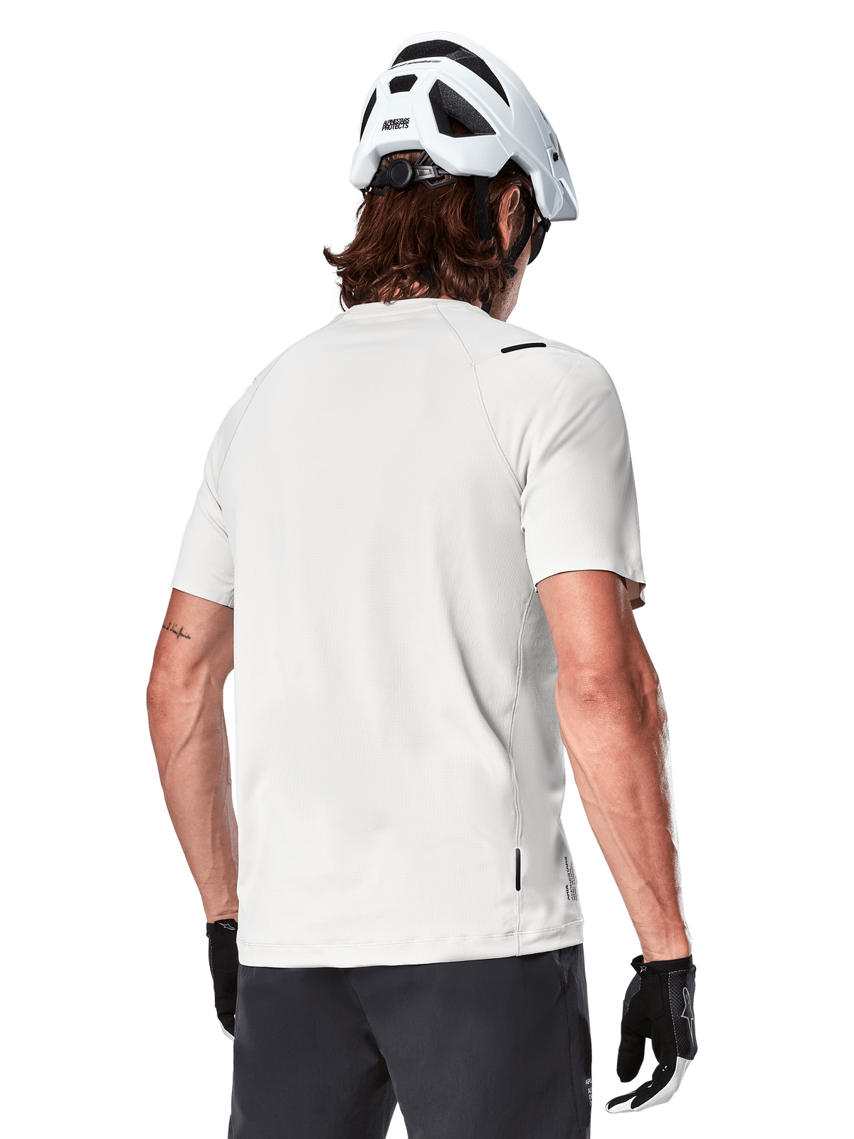 Alpinestars A-Aria Astar Jersey, manches courtes, White Dove, vue arrière d'un maillot de VTT léger et respirant, porté avec un casque blanc et des gants de cyclisme noirs, doté d'un pan arrière plus long pour une couverture accrue
