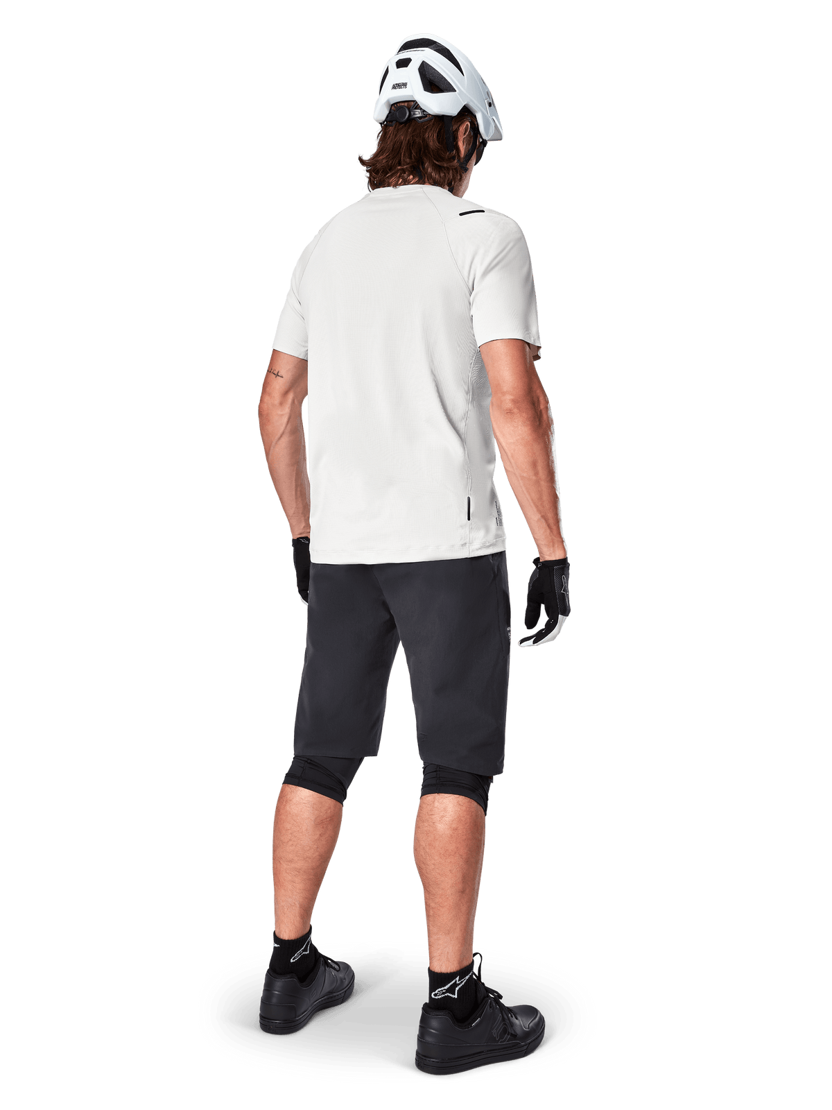 Cycliste portant le maillot à manches courtes Alpinestars A-Aria Astar en White Dove, vue arrière, associé à un short de VTT noir, des genouillères et un casque blanc, équipement léger et respirant pour le VTT tout-terrain