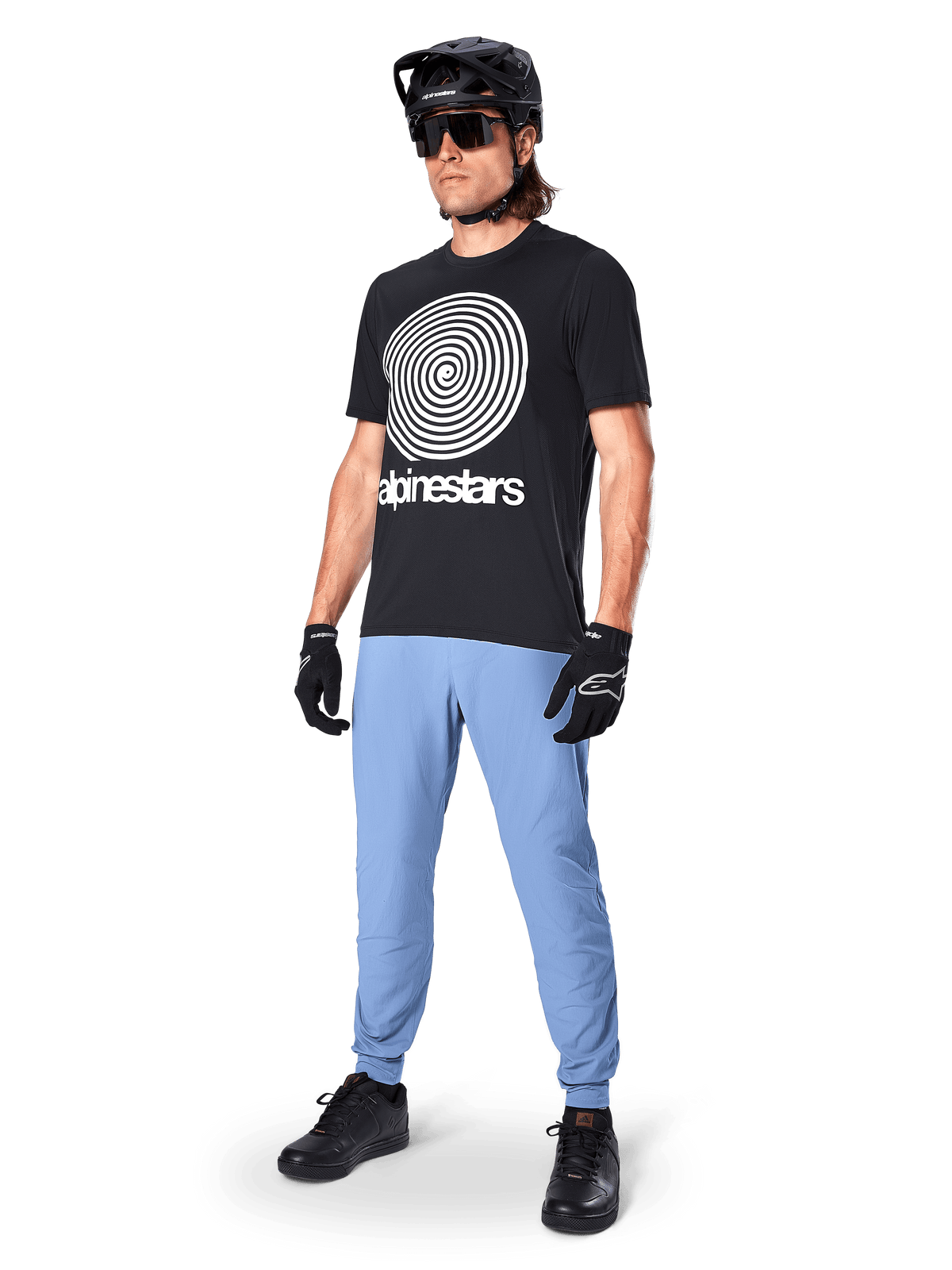 Maillot à manches courtes Alpinestars A-Dura Oscar, maillot de VTT noir avec un grand graphique en spirale blanc vintage, porté par un cycliste avec un casque noir, des lunettes de soleil, des gants noirs et un pantalon bleu clair, équipement de VTT haute performance