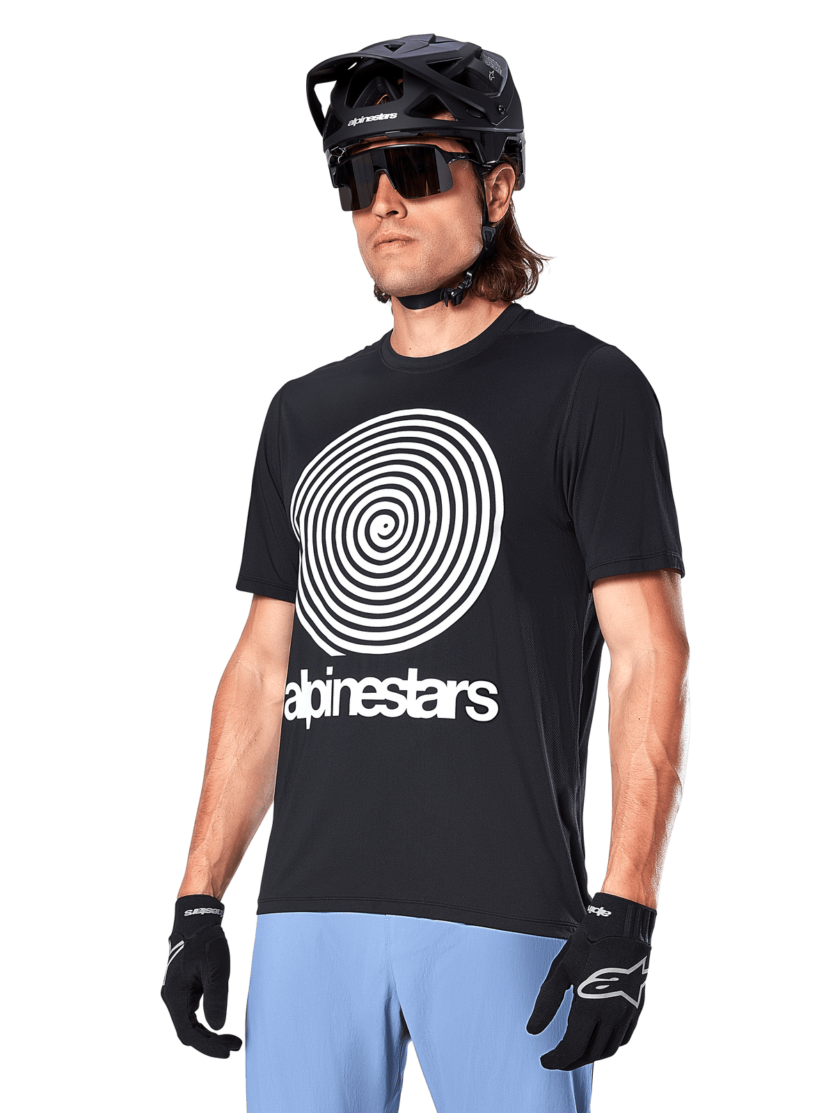 Maillot Alpinestars A-Dura Oscar - Manches courtes, noir, avec un grand graphique en spirale blanc et le logo Alpinestars sur la poitrine, porté par un cycliste avec un casque de VTT noir, des lunettes de soleil et un pantalon bleu clair