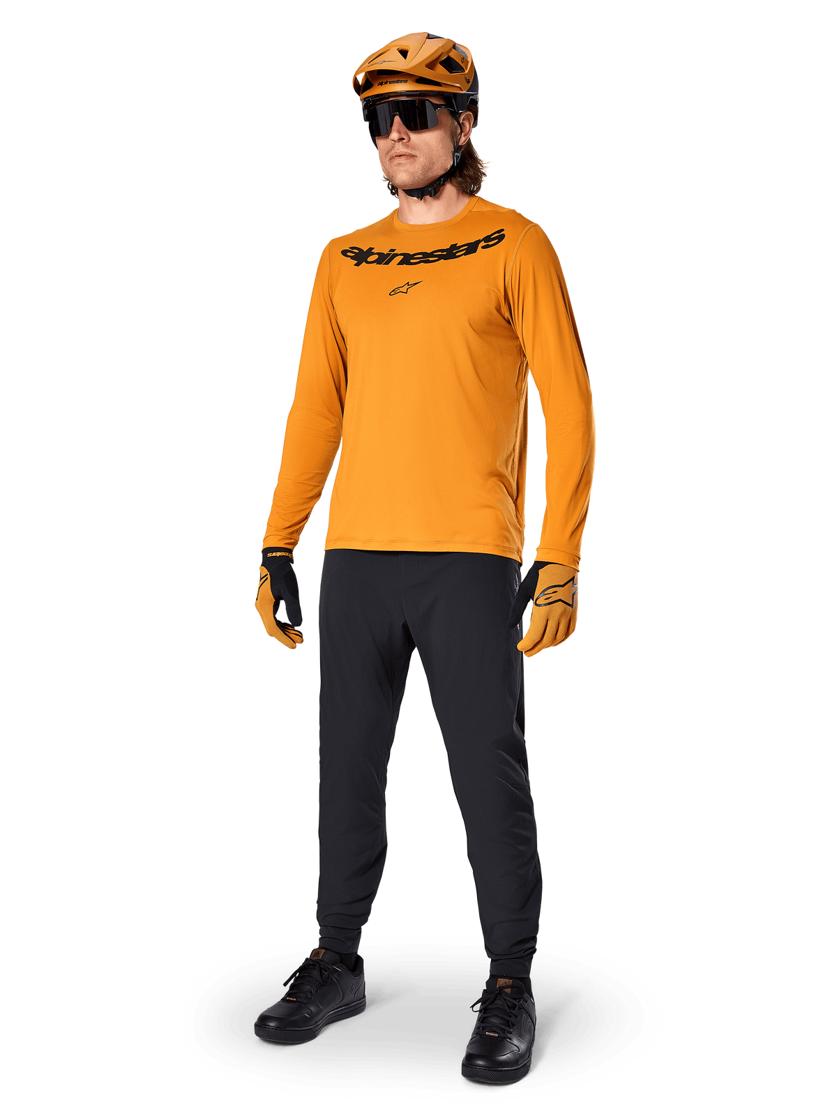 Maillot à manches longues Alpinestars A-Dura Rocker, maillot de cyclisme or foncé, porté avec un casque de VTT assorti et un pantalon noir, orné d'un logo lettrage noir sur la poitrine, équipement de performance coordonné pour le VTT tout-terrain