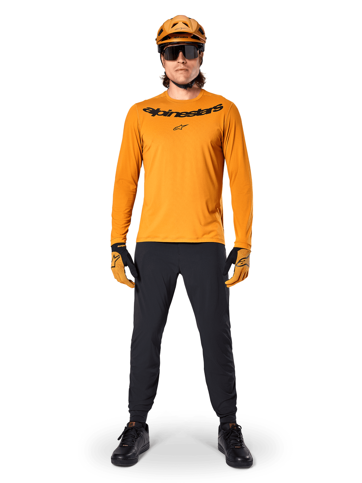 Maillot à manches longues Alpinestars A-Dura Rocker en Or foncé, avec logo noir sérigraphié sur la poitrine, porté avec un casque de VTT doré assorti, des lunettes de soleil noires et un pantalon noir, équipement de VTT professionnel