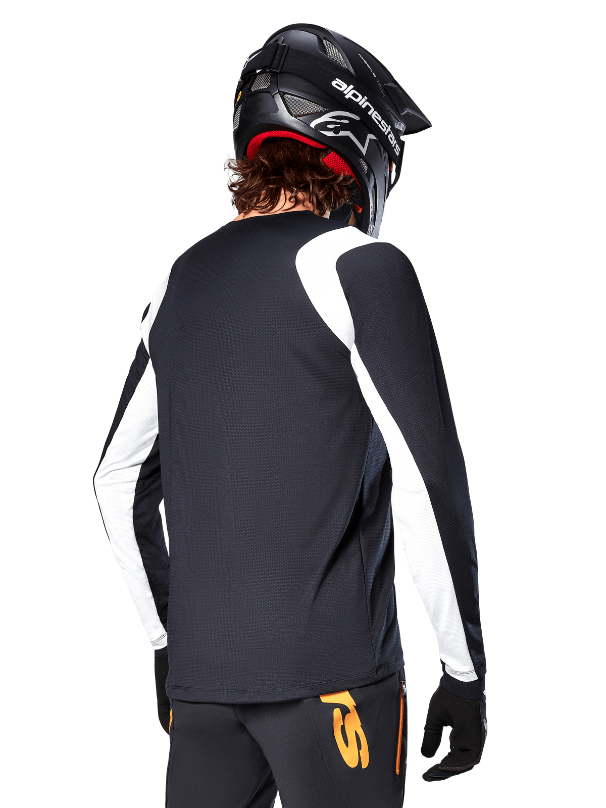 Cycliste de VTT portant un maillot à manches longues Alpinestars A-Supra Oscar, noir avec des empiècements blancs sur les épaules et les manches, vue de dos, casque et gants noirs, pantalon avec des touches d'orange, équipement de cyclisme tout-terrain durable