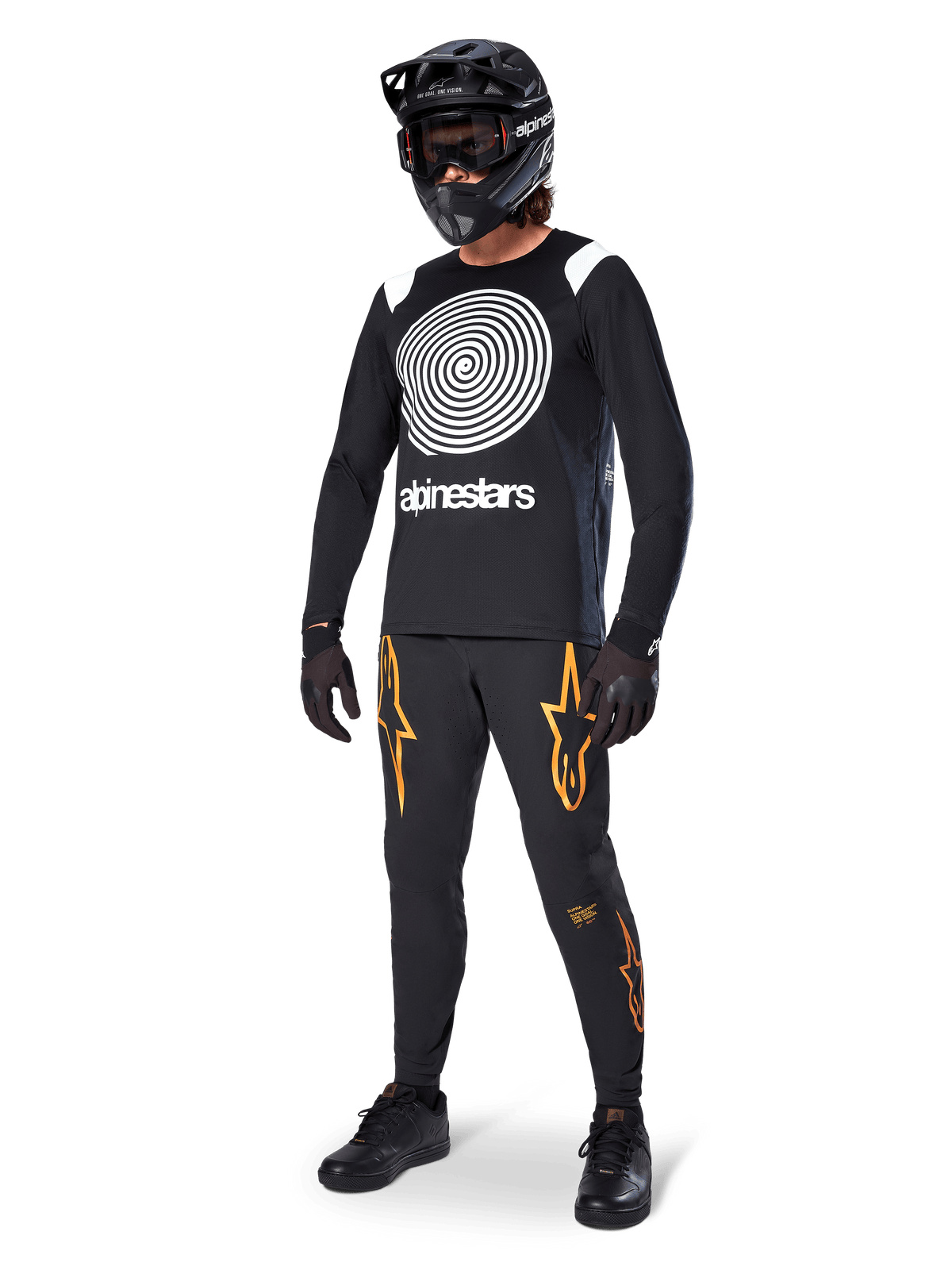 Cycliste de VTT portant le maillot à manches longues Alpinestars A-Supra Oscar noir, graphique en spirale Oscar vintage blanc, pantalon noir avec logos d'étoiles orange, casque intégral noir avec masque et gants noirs, équipement de VTT professionnel