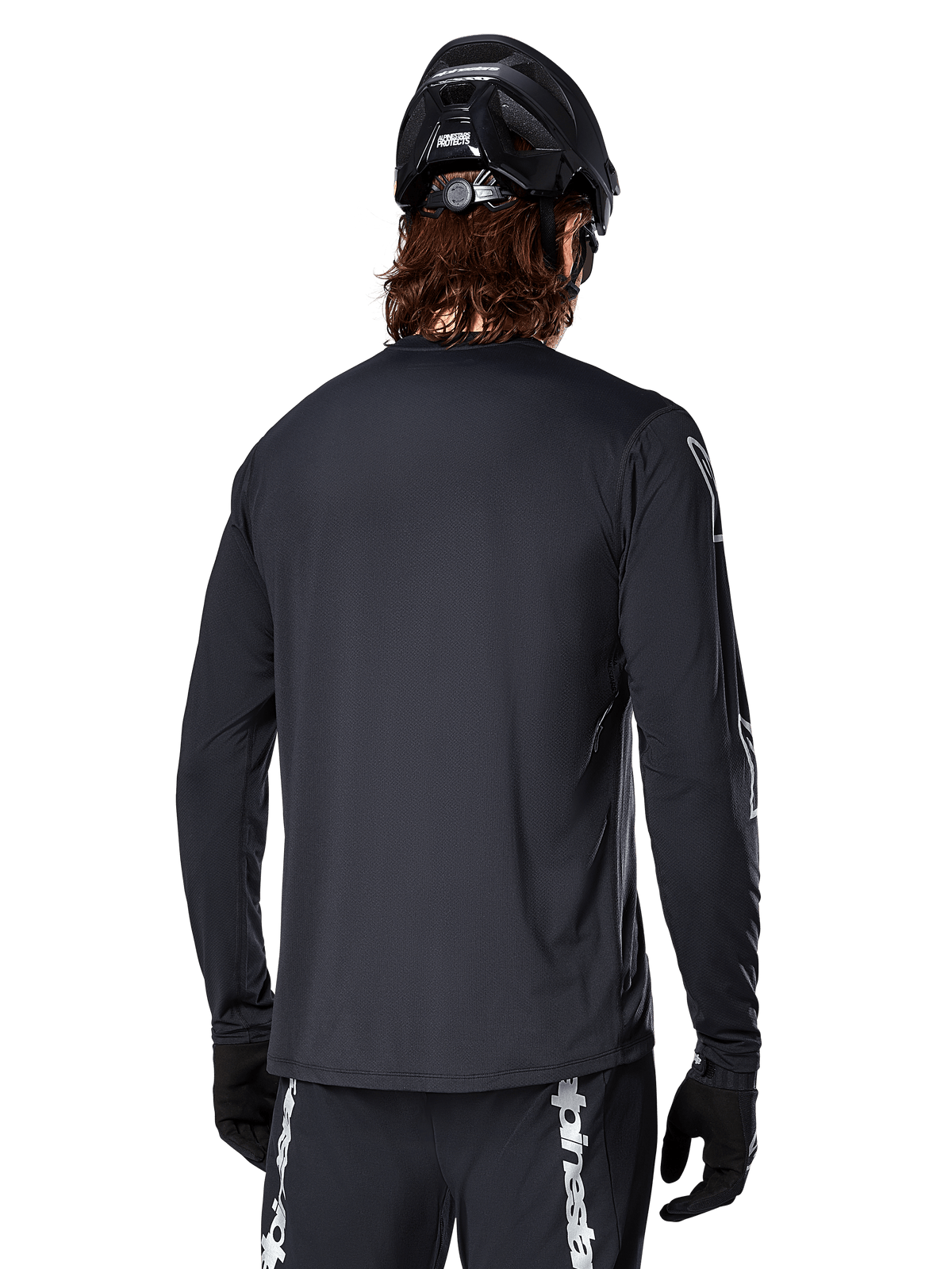 Maillot à manches longues Alpinestars A-Dura Switch, noir, vue arrière sur un cycliste portant un casque de VTT noir et des gants, doté d'un tissu jacquard technique et d'une coupe allongée dans le dos pour la pratique du tout-terrain