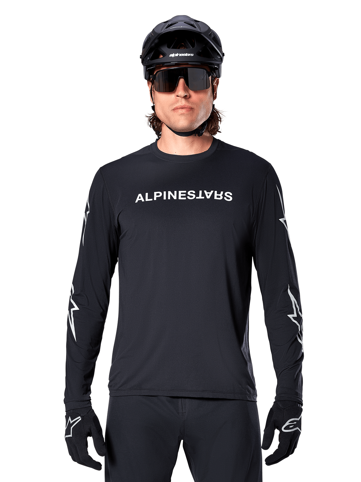 Maillot à manches longues Alpinestars A-Dura Switch, maillot de VTT noir, logo Alpinestars blanc sur la poitrine et graphismes d'étoiles sur les manches, porté avec un casque de VTT noir et des lunettes de soleil de performance, vêtement technique de trail