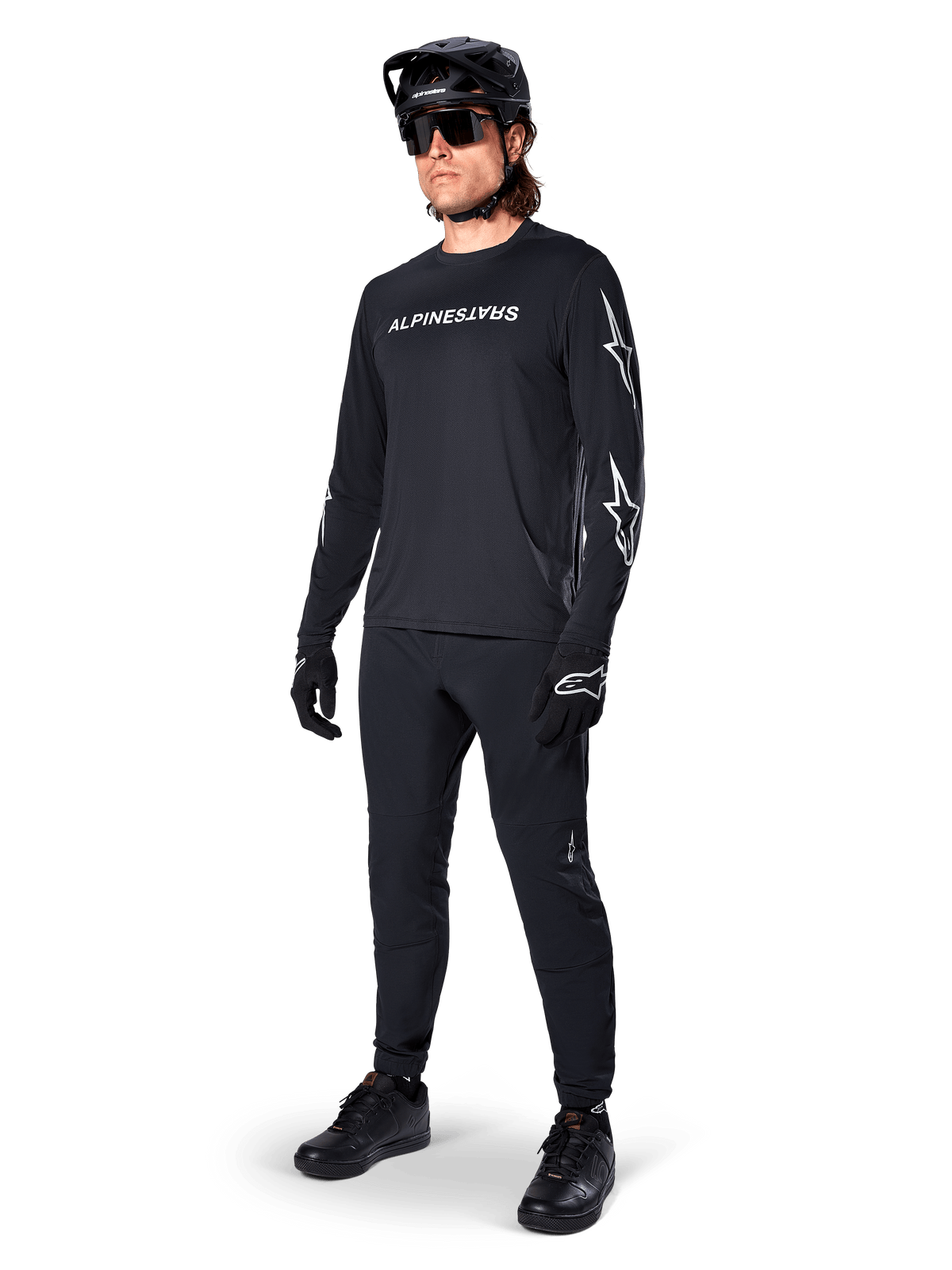 Maillot à manches longues Alpinestars A-Dura Switch, noir, maillot de VTT porté avec un pantalon, un casque et des gants noirs, avec logo lettrage blanc sur la poitrine et logos étoiles sur les manches, équipement de VTT coordonné pour le tout-terrain
