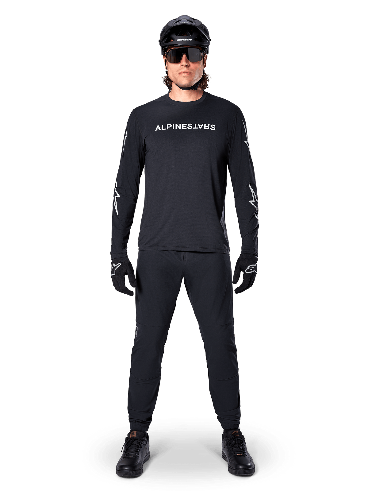 Maillot à manches longues Alpinestars A-Dura Switch, noir, porté par un cycliste de VTT avec pantalon et casque noirs assortis, arborant un logo textuel blanc sur la poitrine, vêtement technique de cyclisme tout-terrain