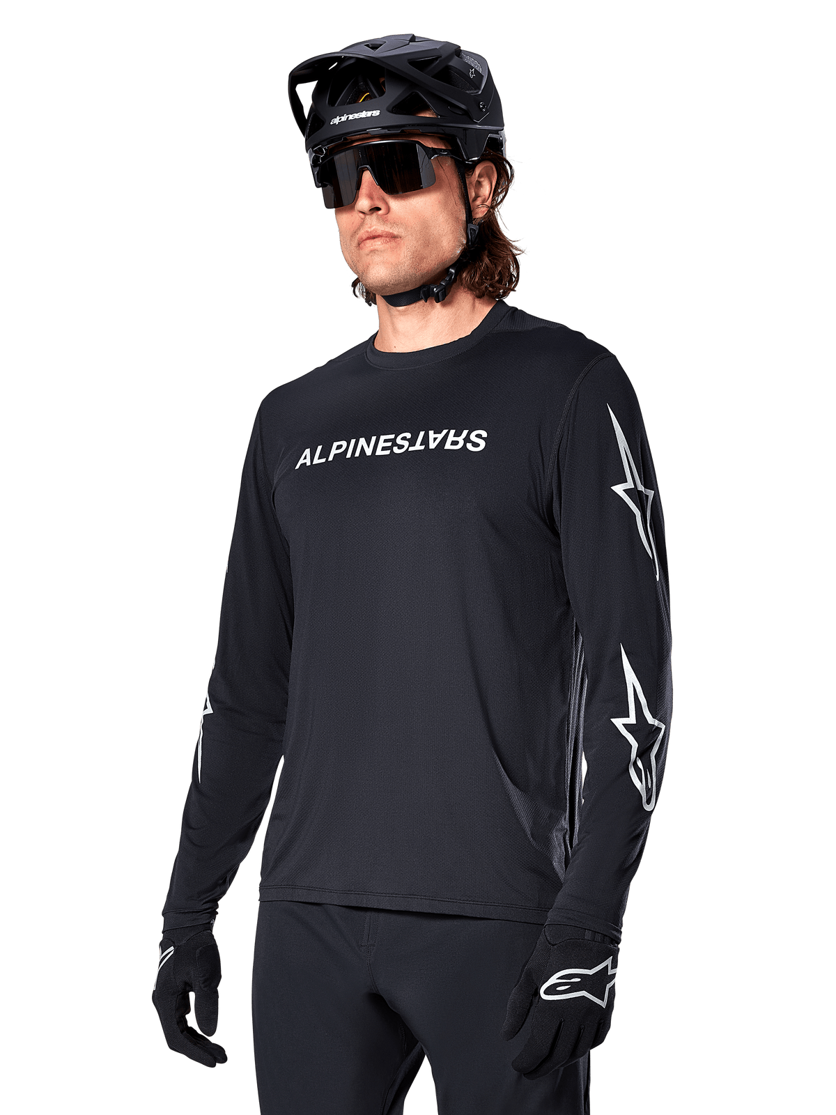 Cycliste masculin portant le maillot à manches longues Alpinestars A-Dura Switch, noir avec marquage blanc et logos étoiles sur les manches, avec casque de VTT noir et lunettes de soleil, équipement de cyclisme haute performance pour le tout-terrain