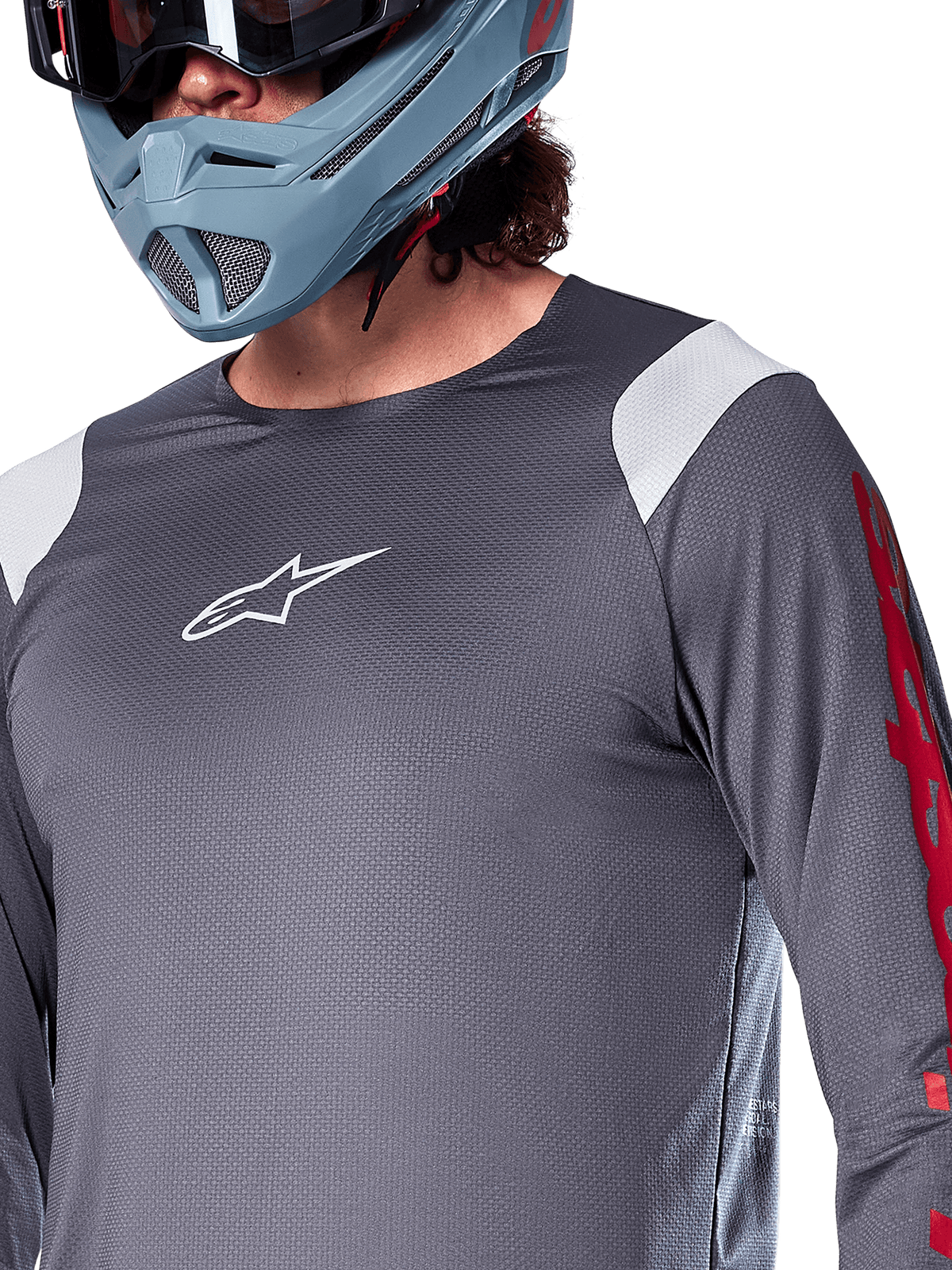 Maillot à manches longues Alpinestars A-Supra Astar, gris foncé avec empiècements blancs aux épaules et graphismes rouges sur les manches, porté avec un casque intégral bleu-gris clair, équipement de VTT haute performance