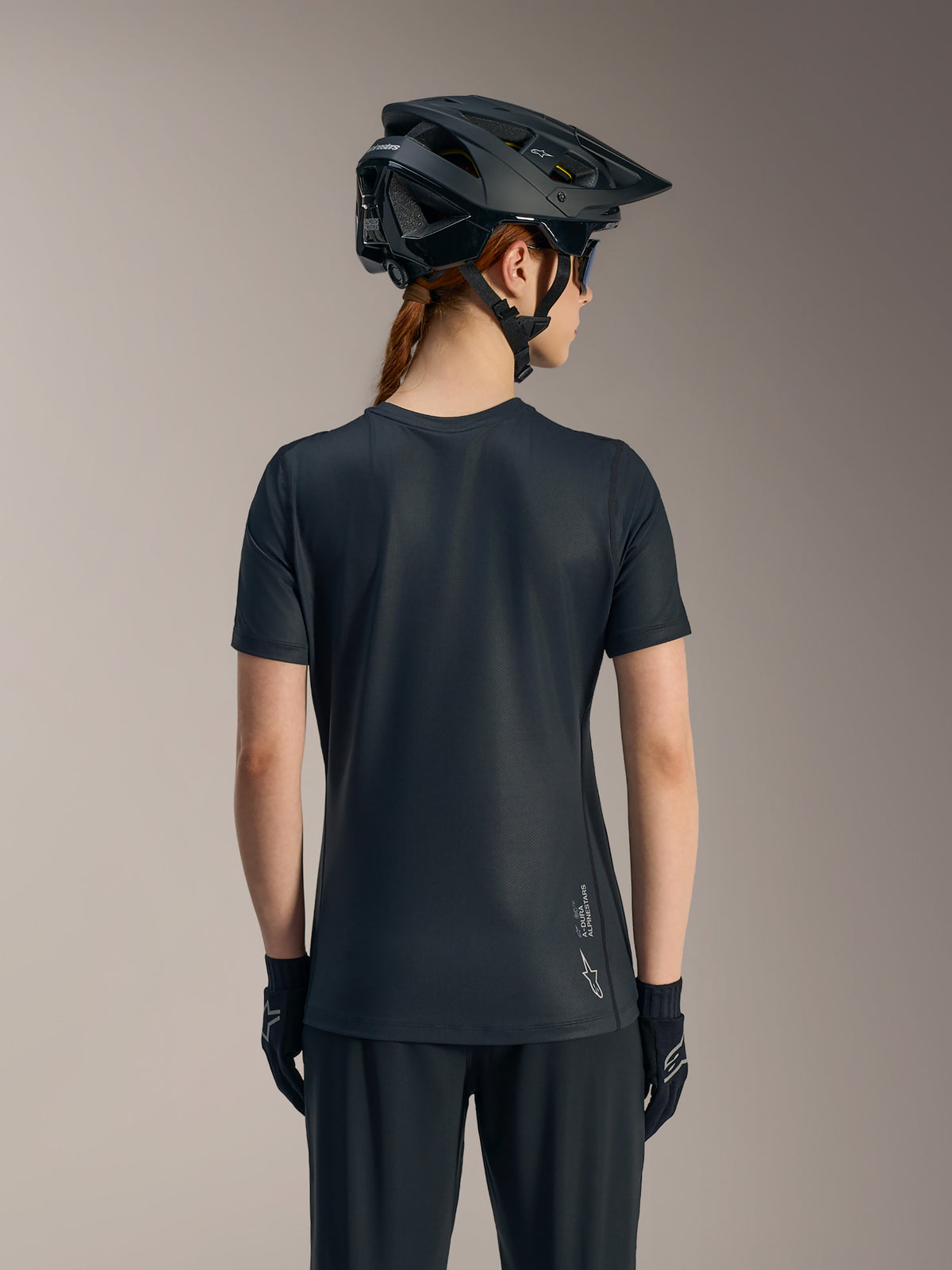 Maillot noir Stella A-Dura Ride femme à manches courtes vu de dos, avec pan arrière long et logo Alpinestars.
