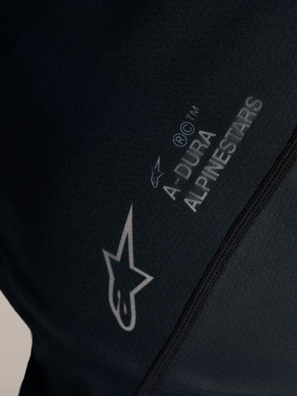 Détail du maillot VTT Stella A-Dura Ride noir, logo Alpinestars blanc et marquage A-DURA sur tissu jacquard.