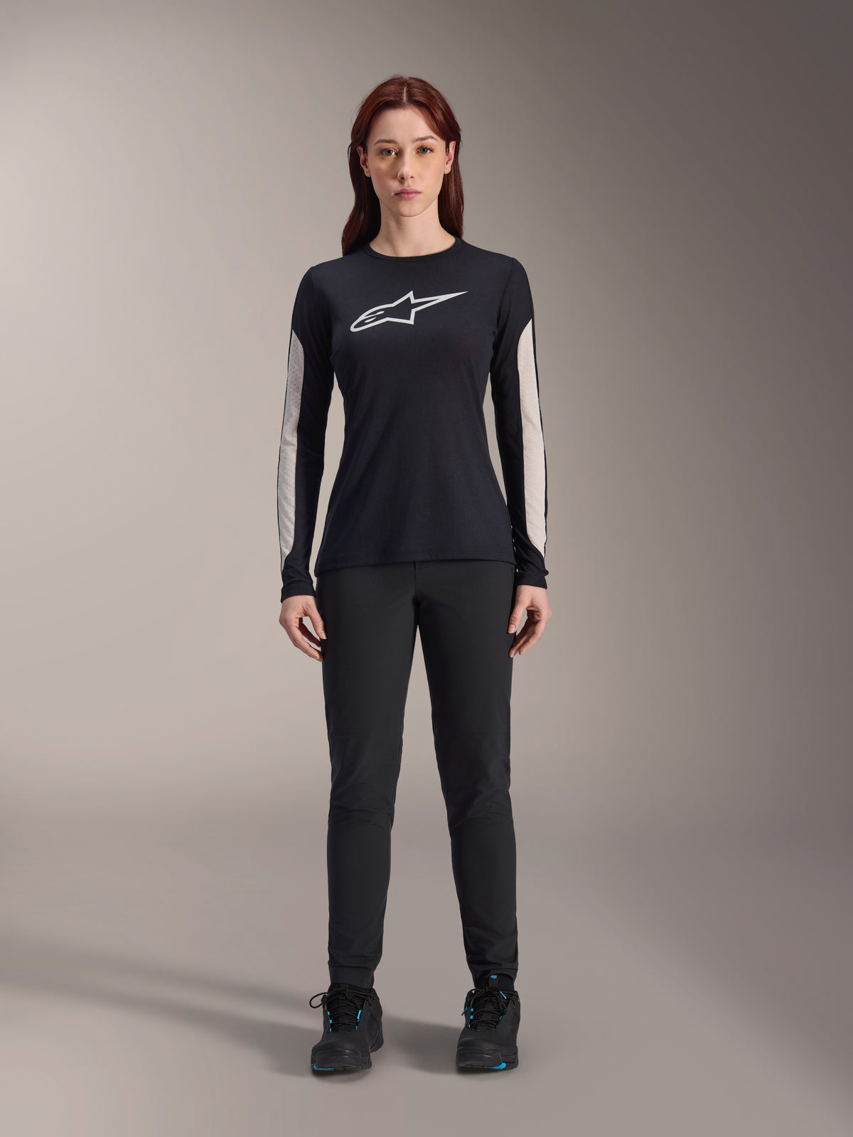 Femme portant le maillot à manches longues Alpinestars Stella A-Dura Dri Astar, noir avec logo blanc sur la poitrine et empiècements en maille claire sur les manches, associé à un pantalon noir et des chaussures noires, vêtement technique de VTT