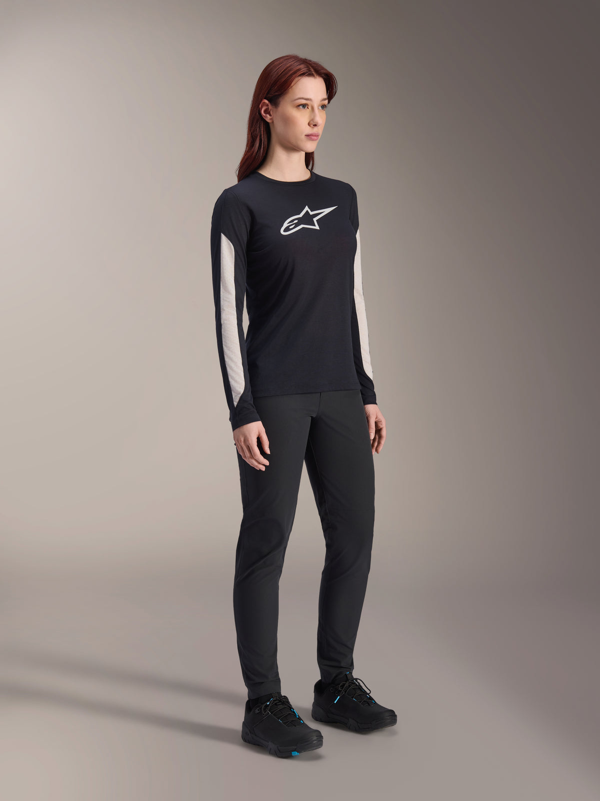 Maillot à manches longues Alpinestars Stella A-Dura Dri Astar pour femme, noir, avec empiècements en maille blanche sur les manches et logo Astar blanc, porté avec un pantalon et des chaussures noirs, vêtement technique de cyclisme pour le VTT