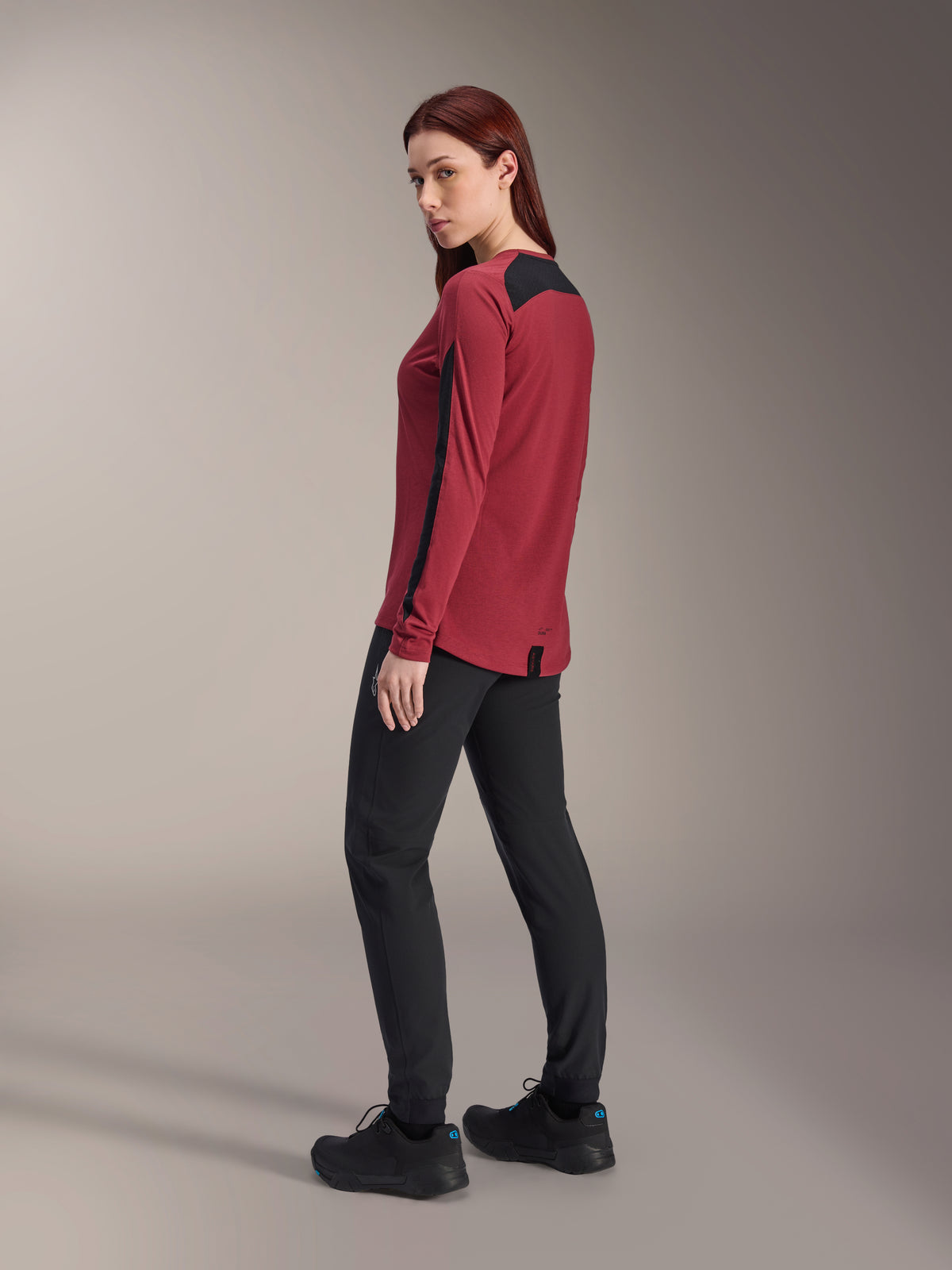 Alpinestars Women Stella A-Dura Dri Astar Long Sleeve Jersey, Burgundy and black, worn with black MTB pants and black shoes, rear-side profile view, recycled drirelease fabric with mesh panels, technical mountain bike apparel