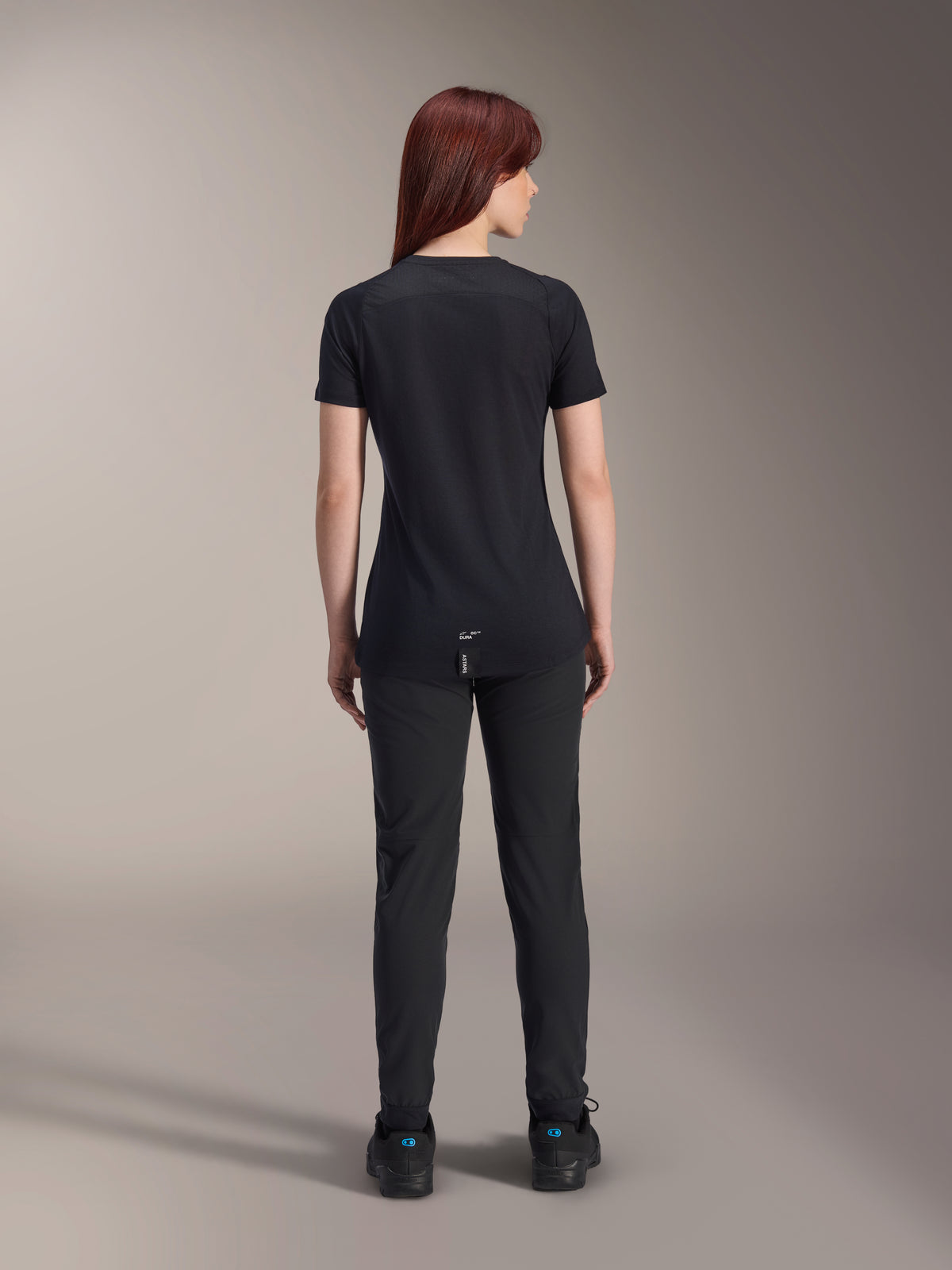 Maillot à manches courtes Alpinestars Stella A-Dura Dri Switch pour femme, noir, vue arrière sur un modèle, avec un pan arrière allongé et des panneaux en maille technique, associé à un pantalon noir, équipement de cyclisme VTT de performance