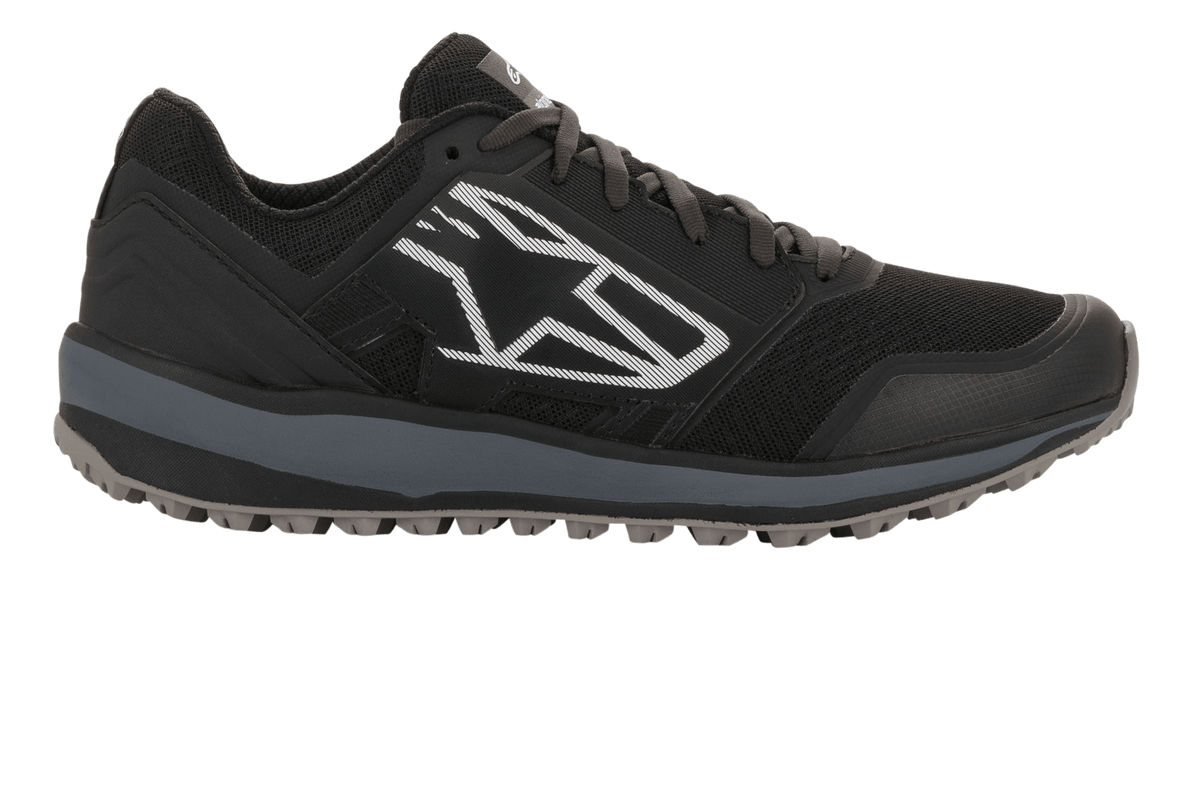 Chaussures Alpinestars Meta Trail, chaussures de course performantes, noir et gris foncé, profil latéral avec un grand logo Astars géométrique blanc, tige en mesh avec semelle intermédiaire grise et semelle en caoutchouc à crampons, chaussures de paddock décontractées pour le sport automobile