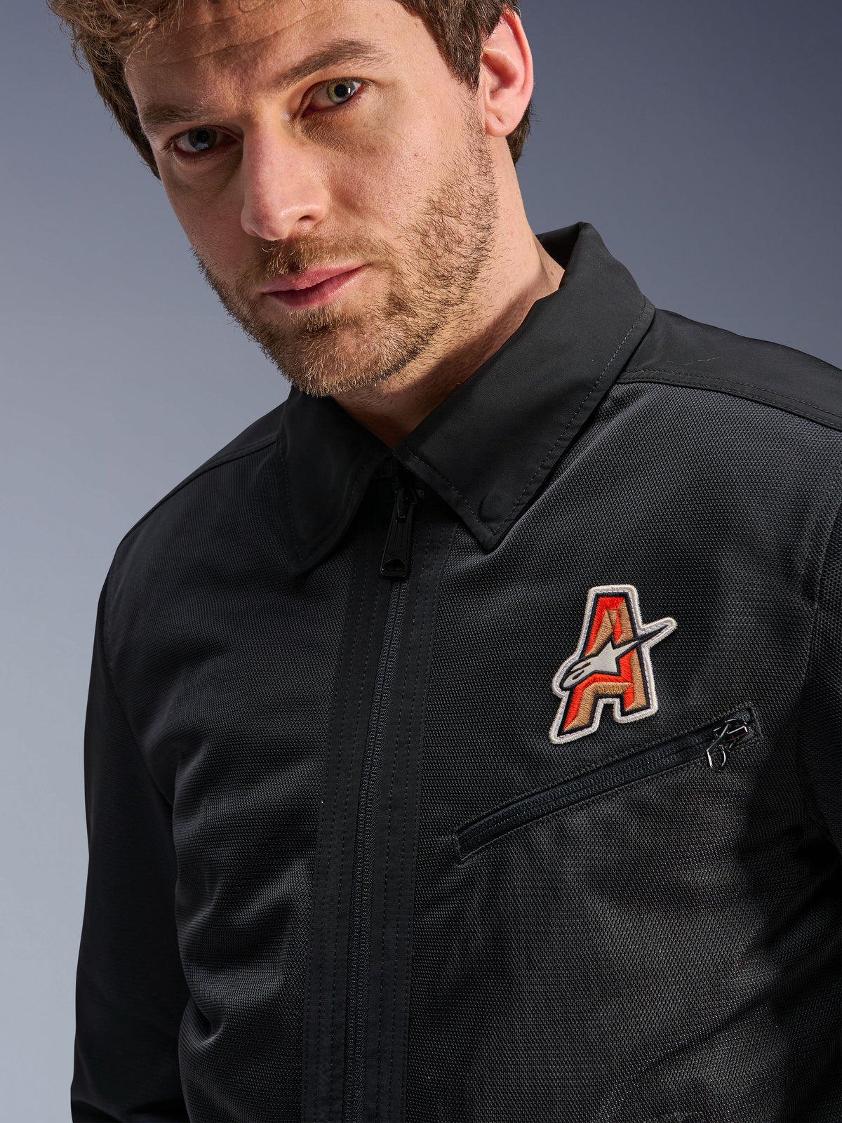 Veste Alpinestars Ignite Air, noire, dotée d'un col de chemise traditionnel et d'une construction en maille respirante, avec un écusson logo « A » rouge et doré sur la poitrine, portée par un mannequin homme, vêtement de moto urbain
