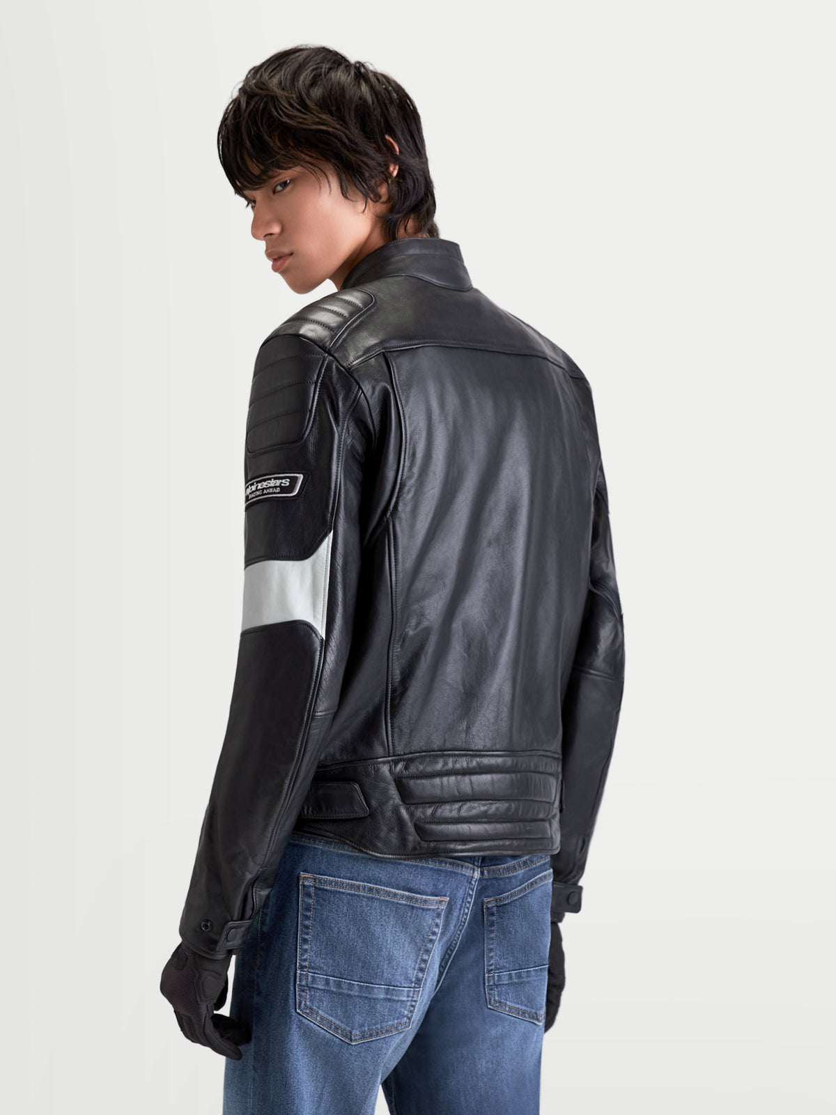 Alpinestars Revern Veste en cuir, blouson de moto urbain pour homme noir et gris métal, vue de dos sur un modèle portant un jean, mettant en valeur la construction en cuir bovin vieilli et le style heritage