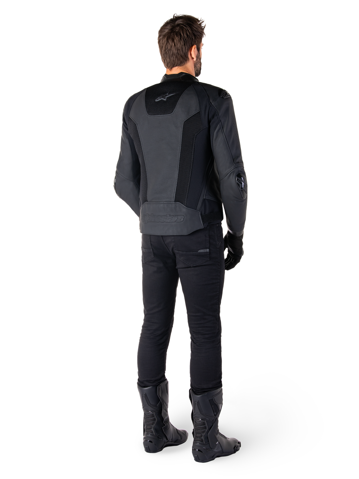 Vue arrière d'un homme portant la veste en cuir Alpinestars Missile V3 Airflow en noir, dotée de larges panneaux perforés pour la ventilation, associée à un pantalon et des bottes de moto noirs, affichant une esthétique de course épurée.