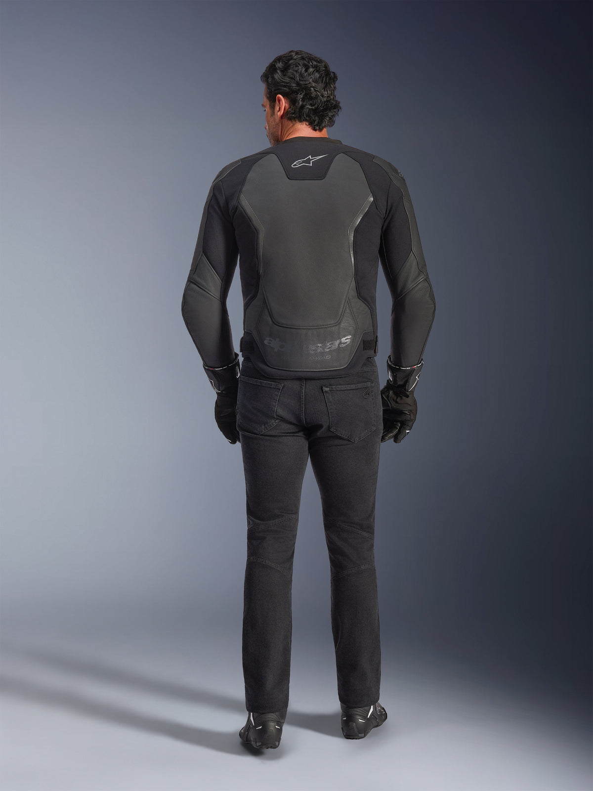 Alpinestars GP Force V2 Leather Jacket, Black, back view, premium sport motorcycle jacket with leather-textile construction, worn with black riding jeans and gloves, featuring protective shoulder panels and branding details