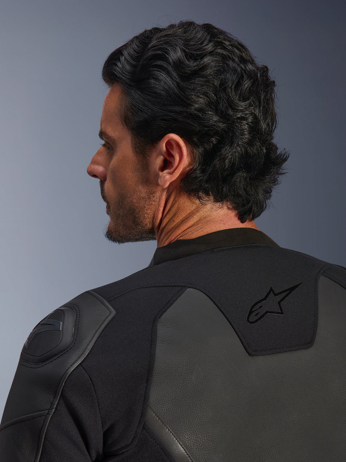 Alpinestars GP Force V2 Leather Jacket, Black, close-up shot from behind, featuring the black star logo on the upper back and GP Lite Evo DFS shoulder protector, multi-panel leather and textile construction, studio view of the rider's profile and gear details.
