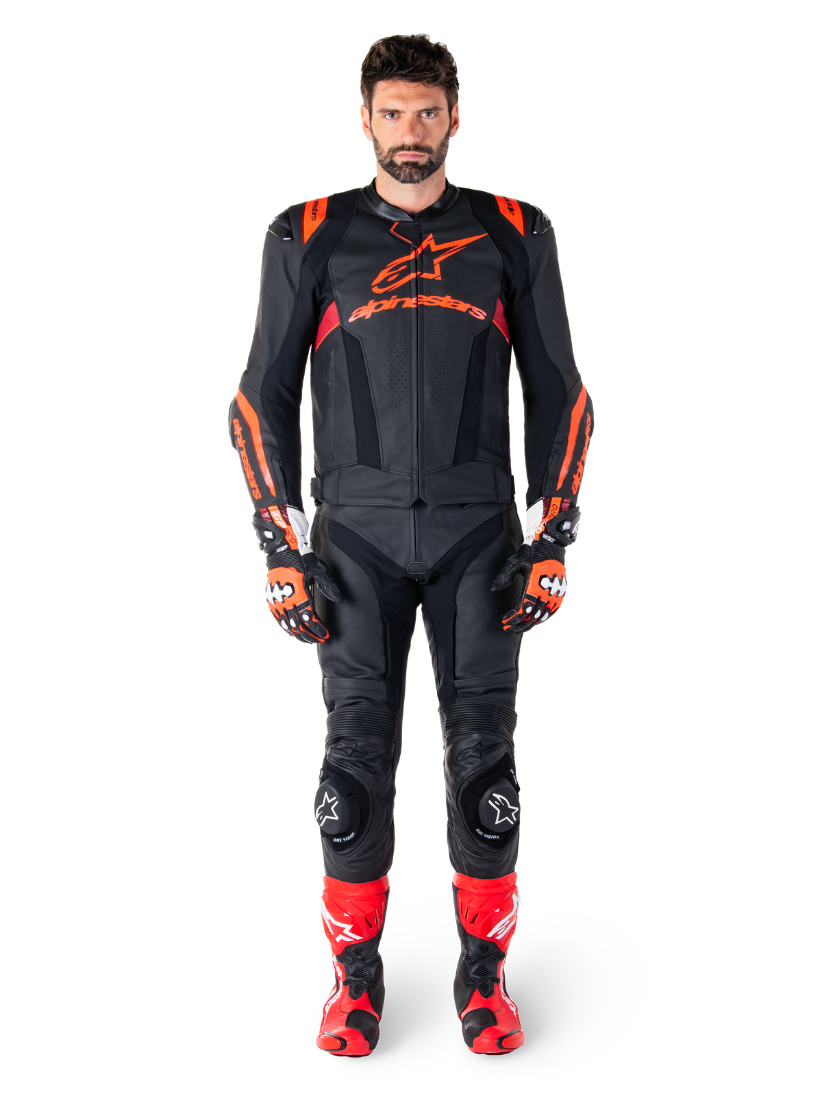Modèle masculin portant la veste en cuir Alpinestars Missile V3 Ignition en Noir Rouge Fluo Rouge Foncé, équipement de moto complet avec pantalon en cuir assorti, gants de course et bottes, logo Alpinestars sur la poitrine, pose de face, tenue de sport professionnelle