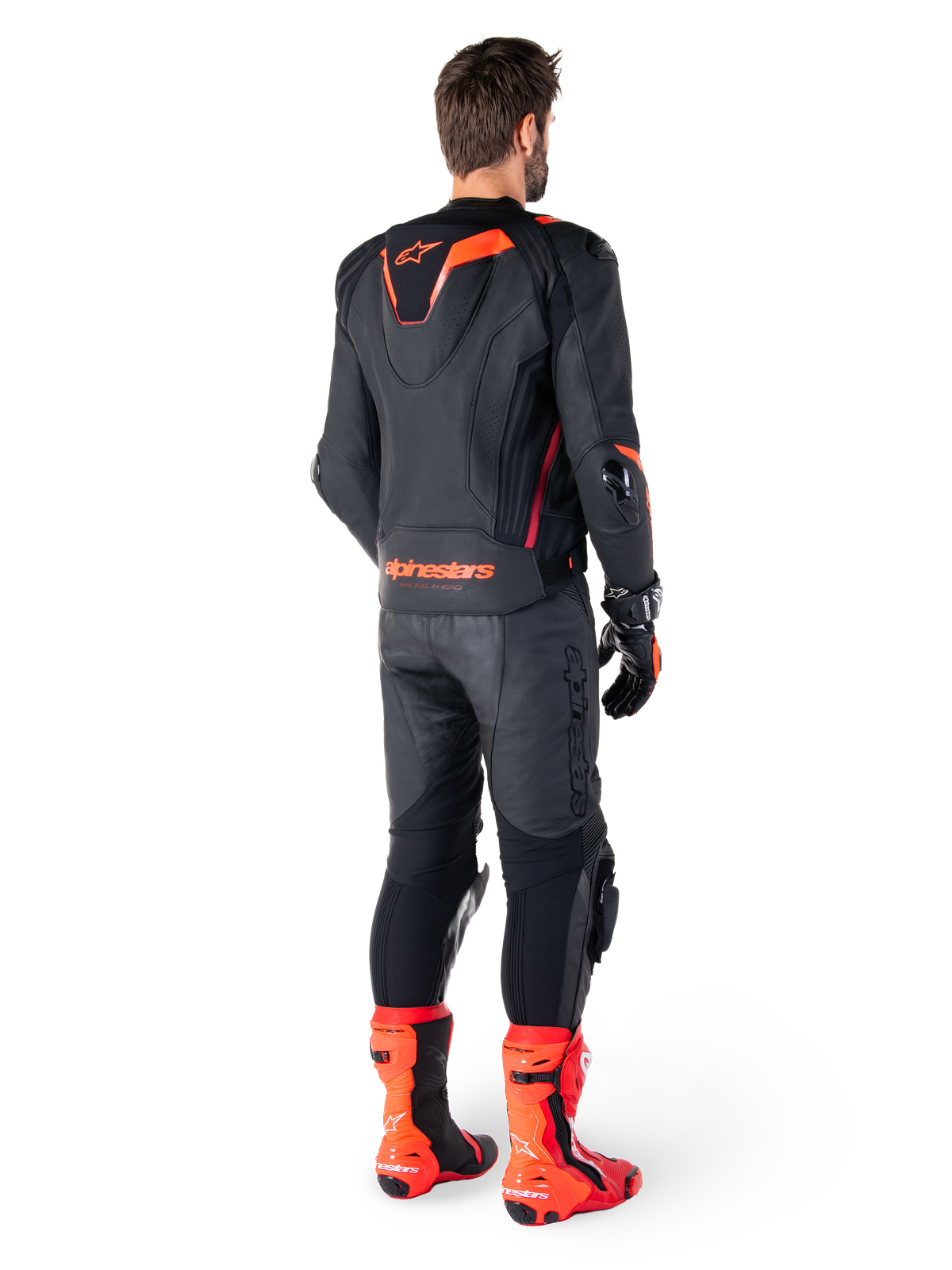Veste en cuir Alpinestars Missile V3 Ignition, veste de moto sport et racing, noir et rouge fluo, vue arrière d'un pilote portant une tenue de course complète avec pantalon en cuir assorti, gants et bottes rouges, dotée d'une bosse aérodynamique sport et d'un marquage distinctif sur le bas du dos.