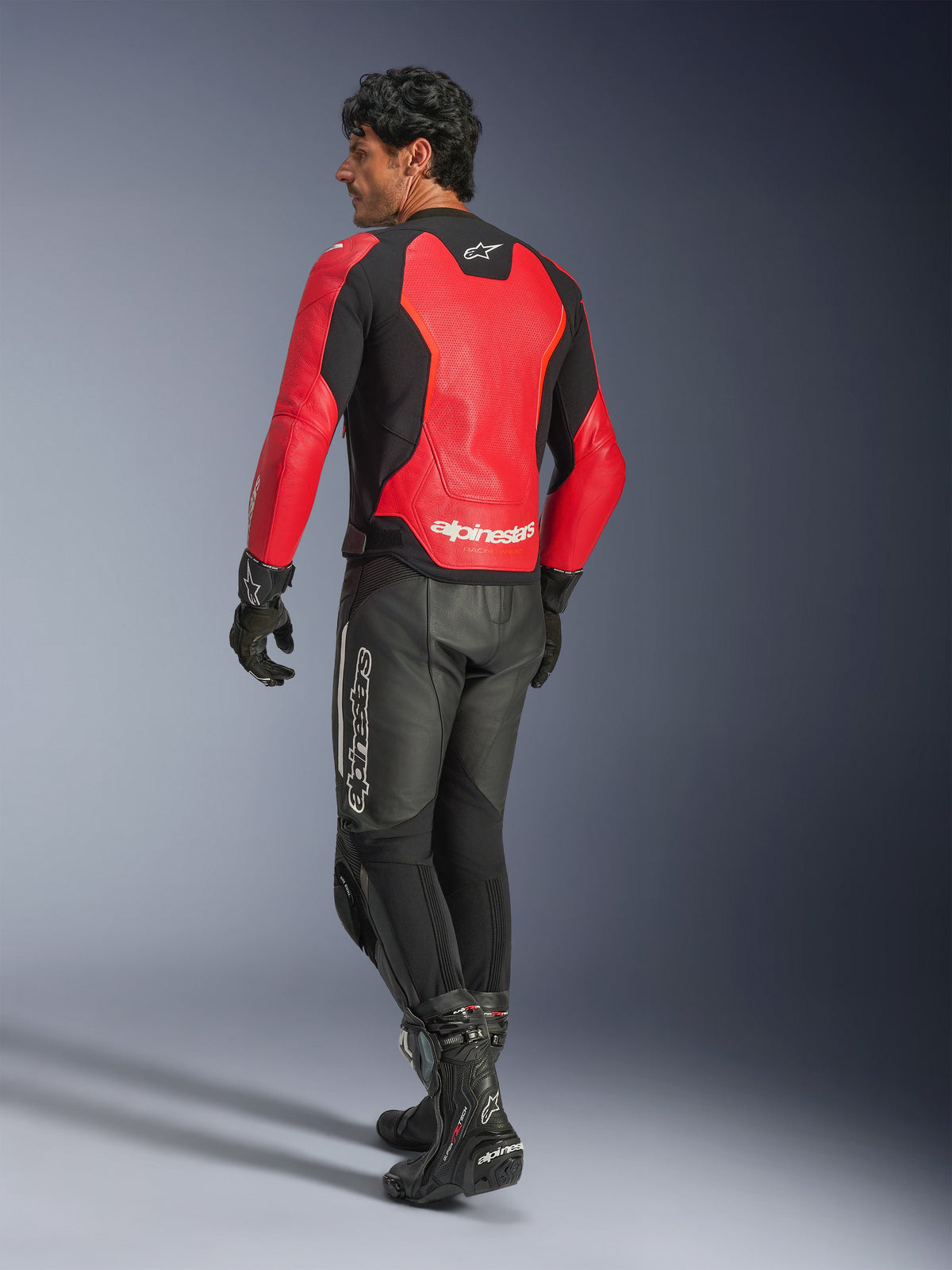 Blouson en cuir Alpinestars GP Force V2 Air, rouge et noir, vue arrière sur un motard, porté avec un pantalon en cuir noir et des bottes de course, avec des panneaux arrière perforés et le logo Alpinestars
