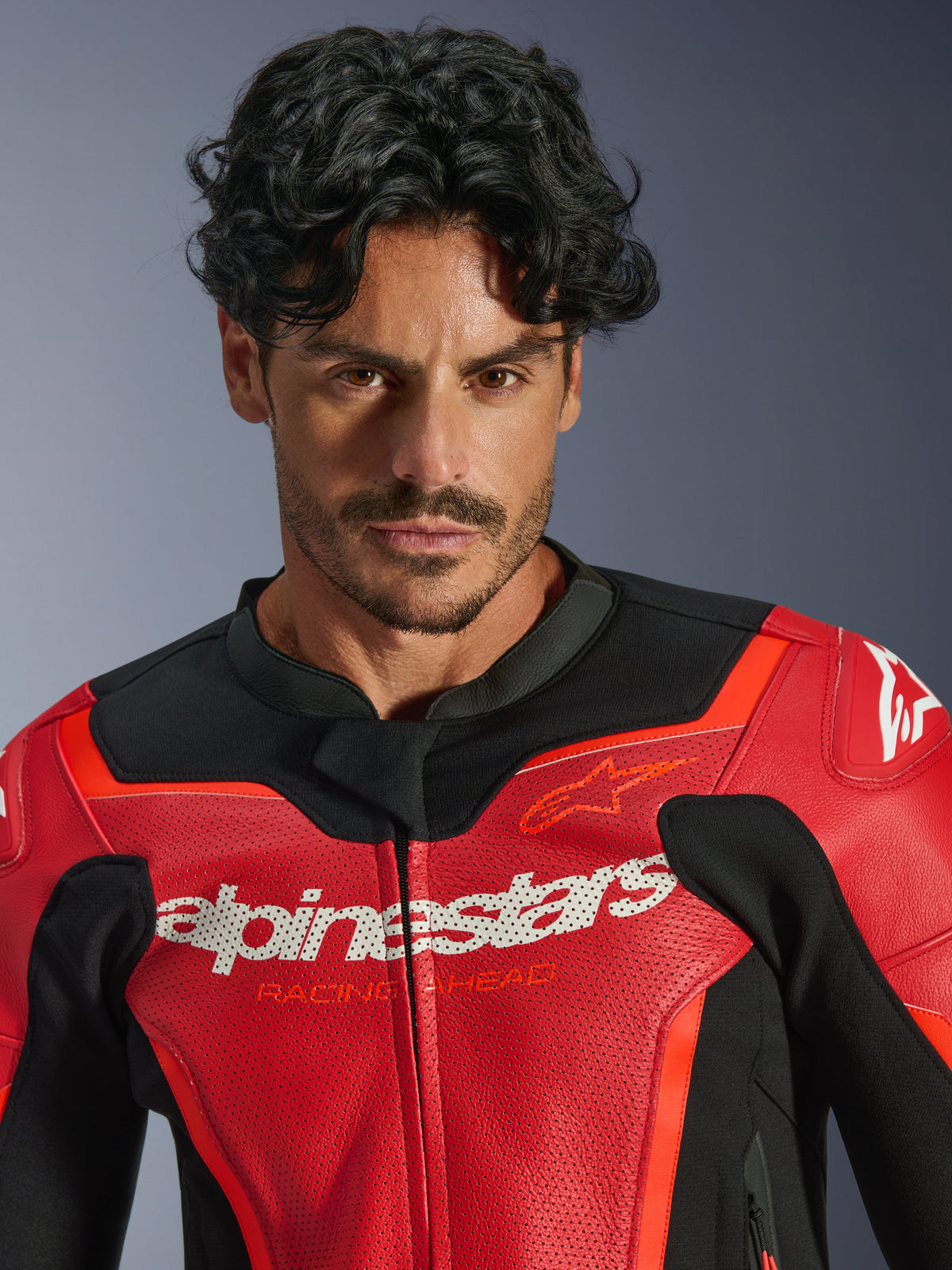 Blouson en cuir Alpinestars GP Force V2 Air, rouge et rouge fluo, porté par un mannequin homme, avec logos Alpinestars et « Racing Ahead » blancs sur la poitrine, cuir perforé pour la circulation de l'air, équipement de moto de style sportif