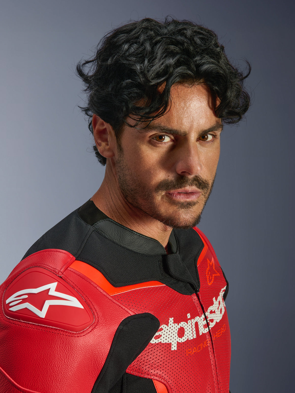 Blouson en cuir Alpinestars GP Force V2 Air, rouge et rouge fluo, porté par un homme dans un portrait en gros-plan, avec cuir de bovin perforé, logos Alpinestars blancs sur la poitrine et l'épaule, et accents en textile noir, équipement de course de moto professionnel