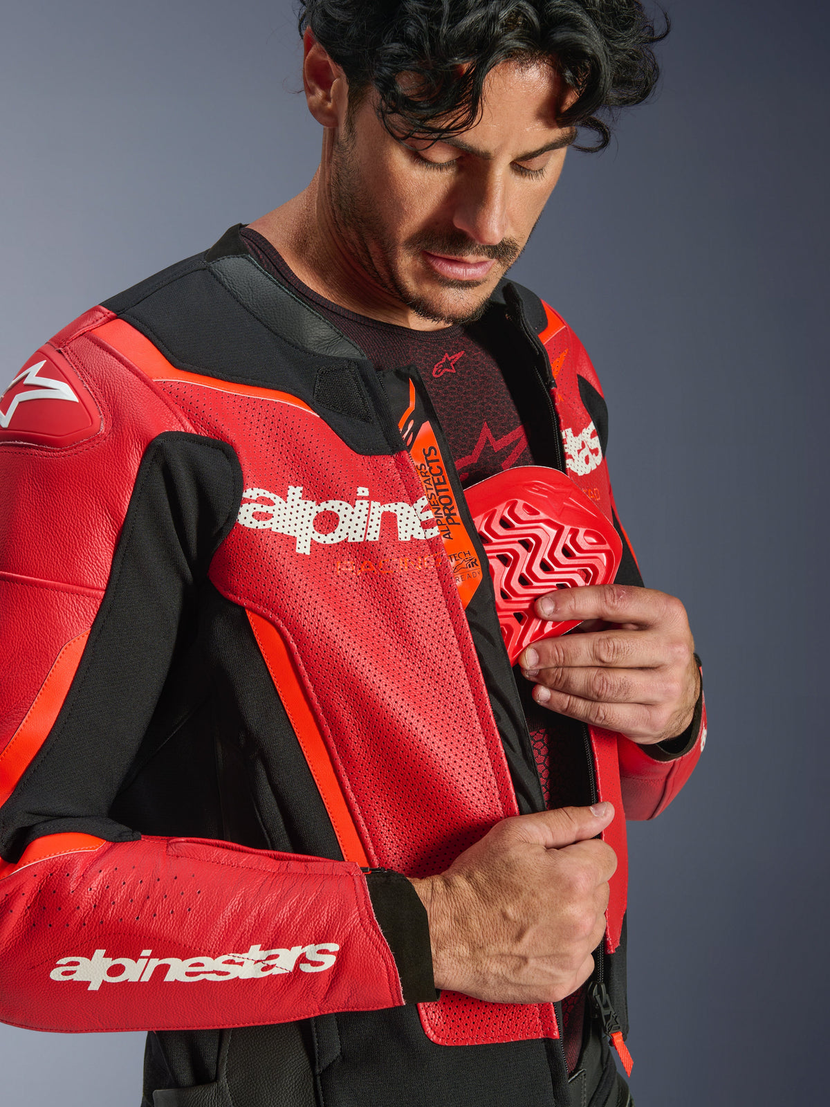 Blouson en cuir Alpinestars GP Force V2 Air, rouge et rouge fluo, gros plan d'un pilote insérant une protection pectorale rouge dans la poche intérieure, doté de cuir perforé et du logo Tech-Air Ready, protection de moto sportive haut de gamme