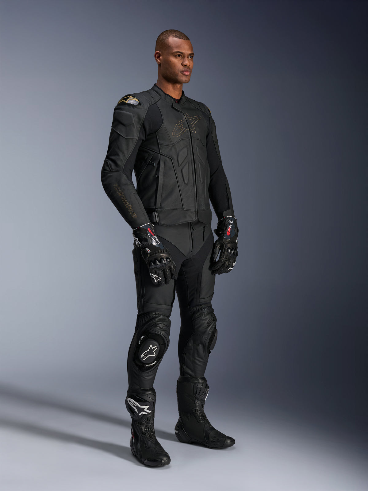 Mannequin homme portant le pantalon en cuir Alpinestars Missile V3 et une veste en cuir noir assortie avec des accents dorés, des gants de course GP Pro noirs et des bottes de course noires, équipement de moto complet pour la route, photo en studio.