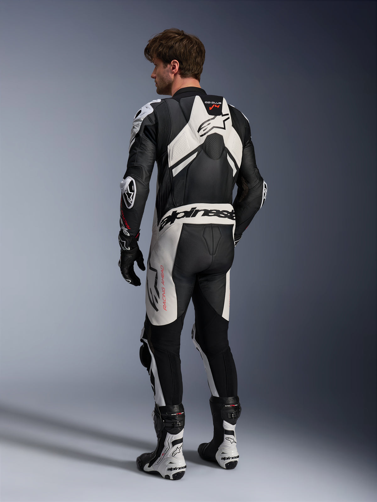 Alpinestars combinaison en cuir GP Plus V4 Sprint 1 pièce pour homme, noire et blanche, technologie A-CS®, certifiée CE AAA, vue arrière d'un pilote avec bosse aérodynamique.