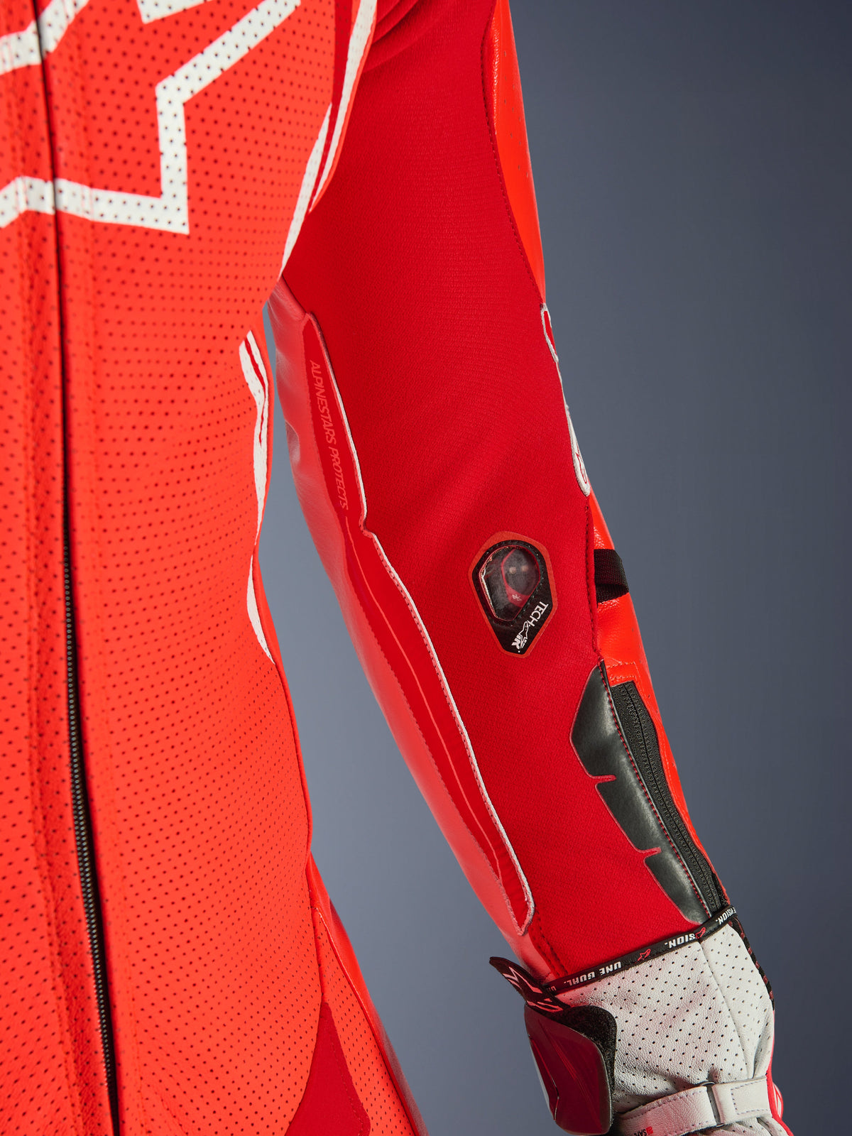 Alpinestars GP Tech V5 One Piece Leather Suit, rouge fluo et rouge vif, gros plan de la manche présentant l'indicateur Tech-Air et des sliders de protection, cuir perforé avec accents blancs, détail d'équipement de course professionnel