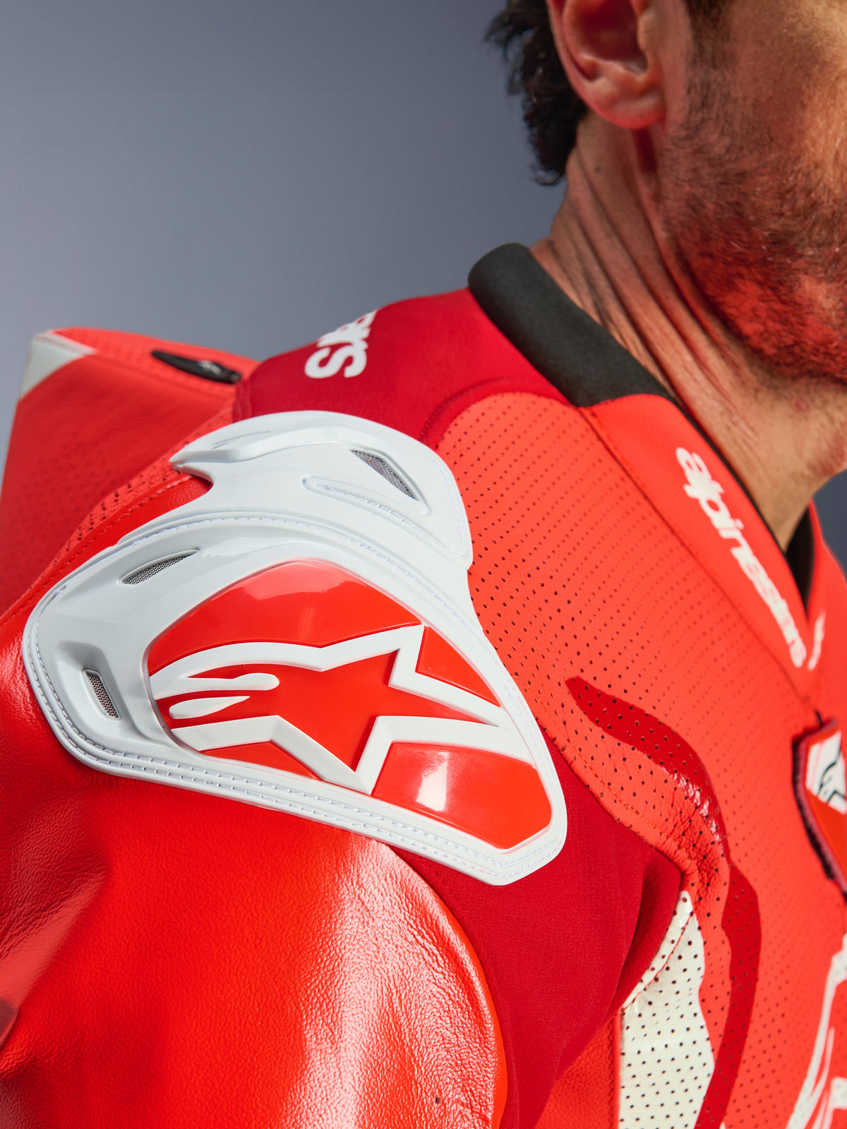 Gros plan de la zone de l'épaule de la combinaison en cuir Alpinestars GP Tech V5 One Piece, Rouge Fluo et Rouge Éclatant, présentant une protection d'impact GP DFS blanche avec un logo étoile rouge et du cuir perforé pour la ventilation.