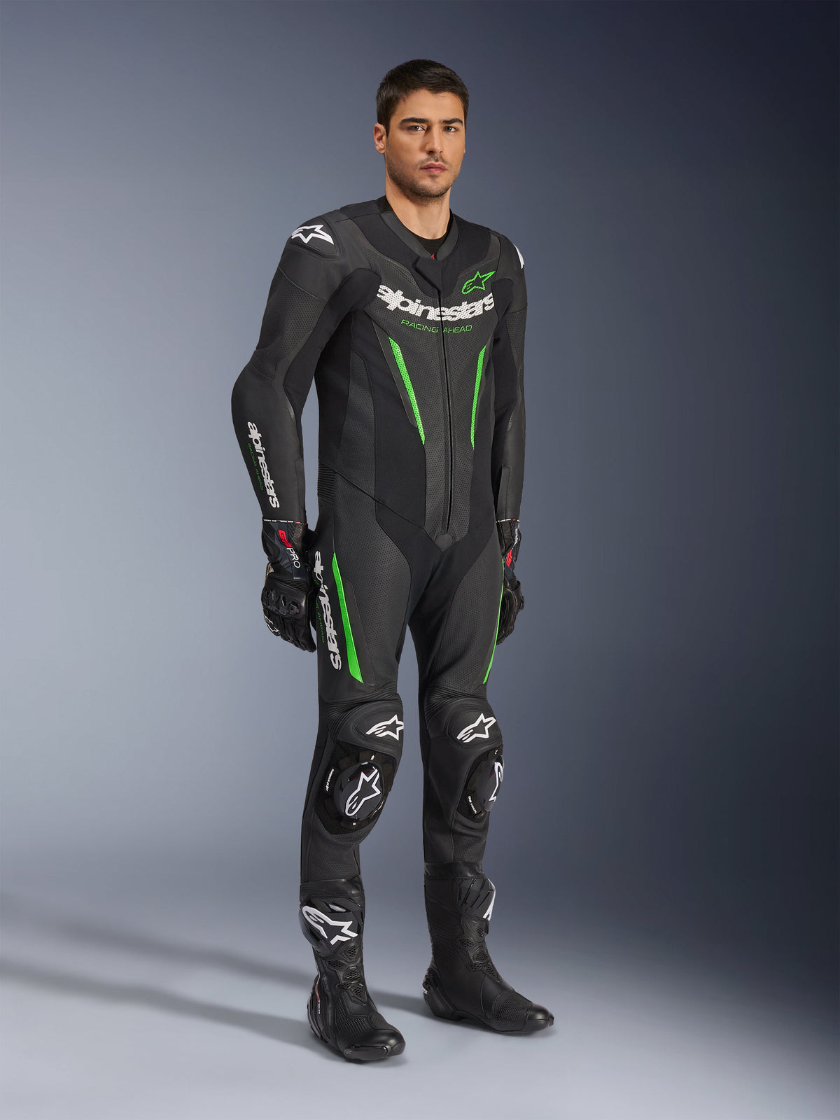 Combinaison en cuir Alpinestars GP Force V2 1 pièce, noir et vert, équipement de course complet porté avec des gants et des bottes noirs, avec panneaux en cuir perforé, logos Alpinestars blancs et sliders de genoux intégrés, tenue de performance professionnelle pour circuit