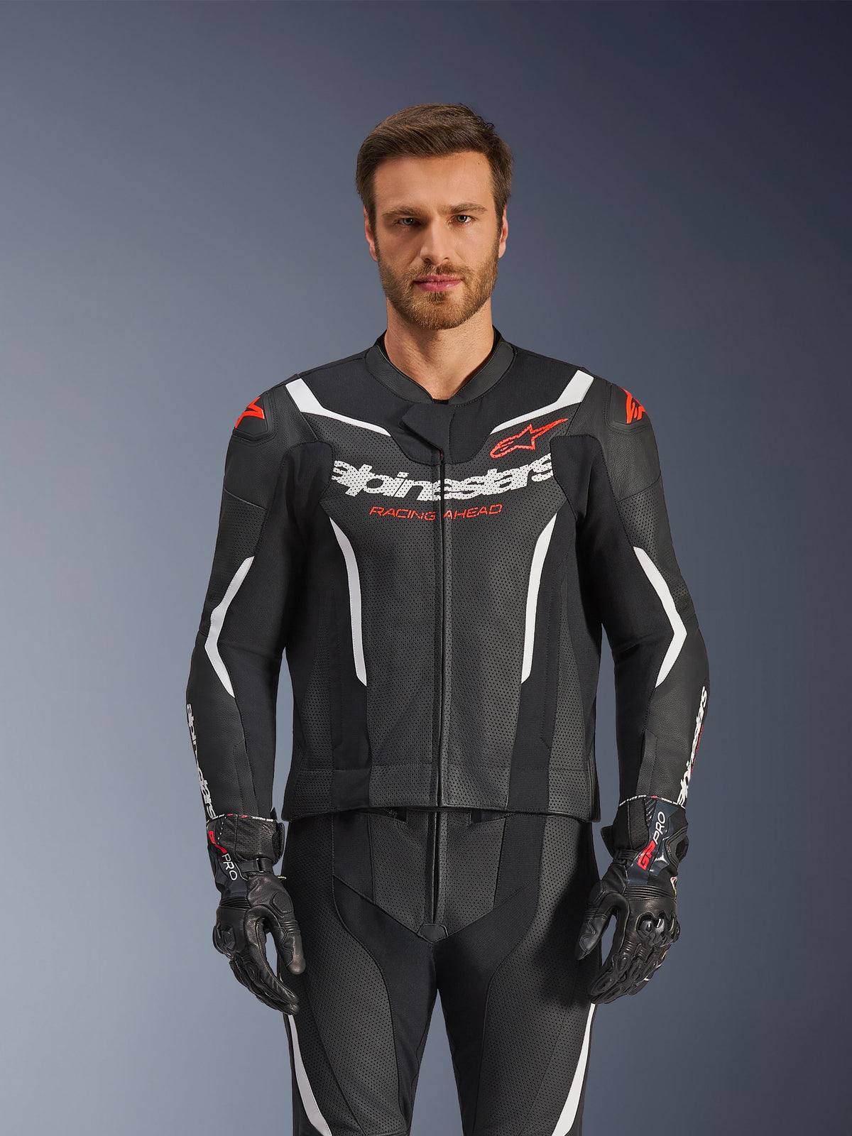 Alpinestars GP Force V2 Leather Suit- 2 pièces, noir, blanc et rouge fluo, vue de face d'un modèle masculin portant la combinaison en cuir perforé avec des gants noirs assortis, présentant des accents angulaires blancs et le logo Alpinestars sur la poitrine